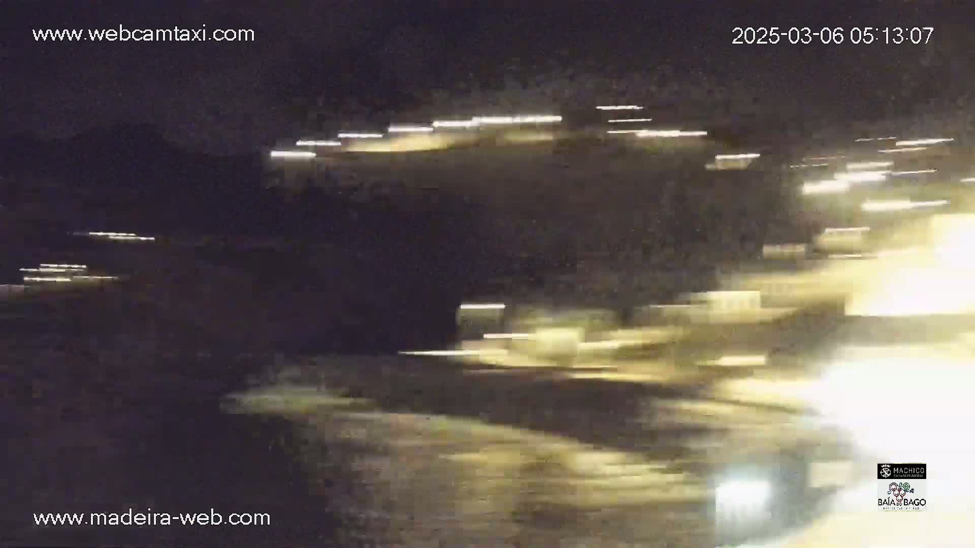 A nighttime long-exposure shot shows streaks of light from vehicles moving along a road in front of a dark hill.