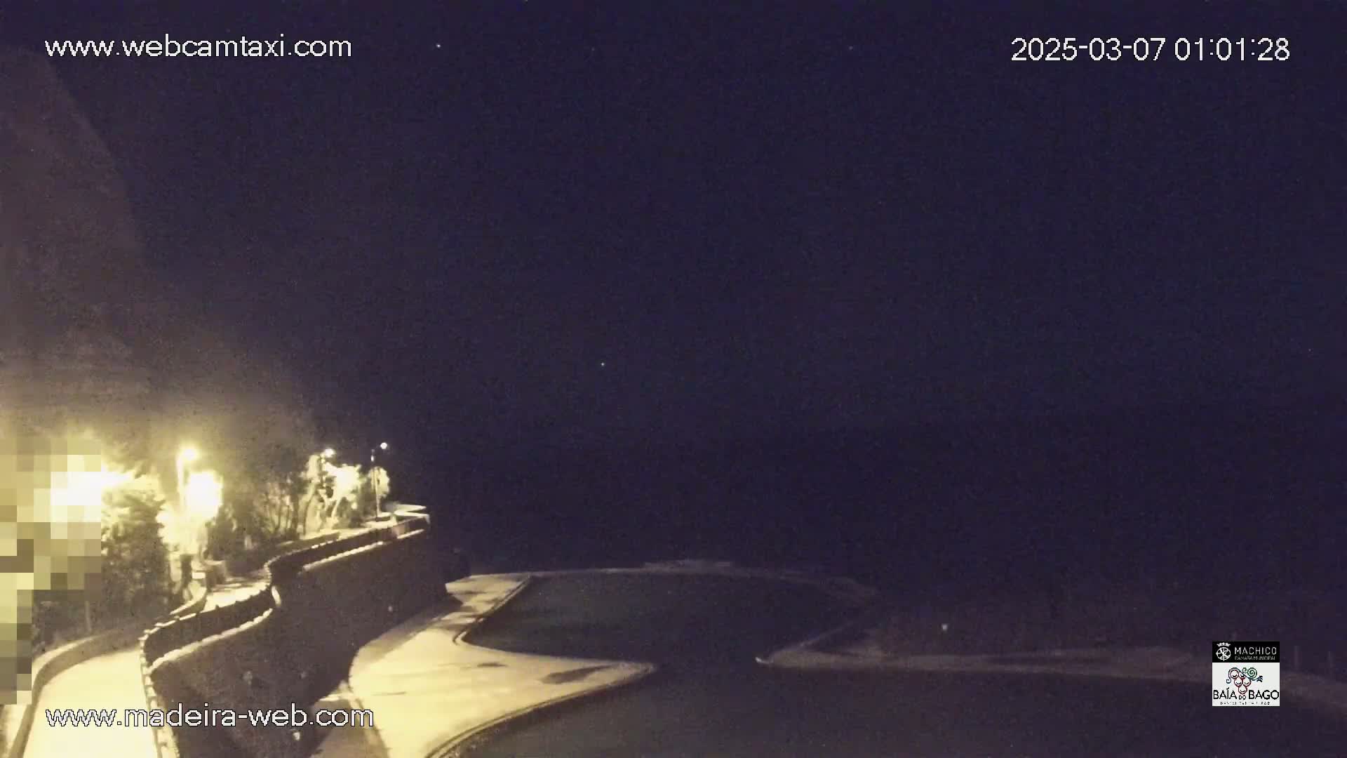 A nighttime view of a snow-covered pool area and a curving stone wall, illuminated by several lights, under a dark, clear sky.