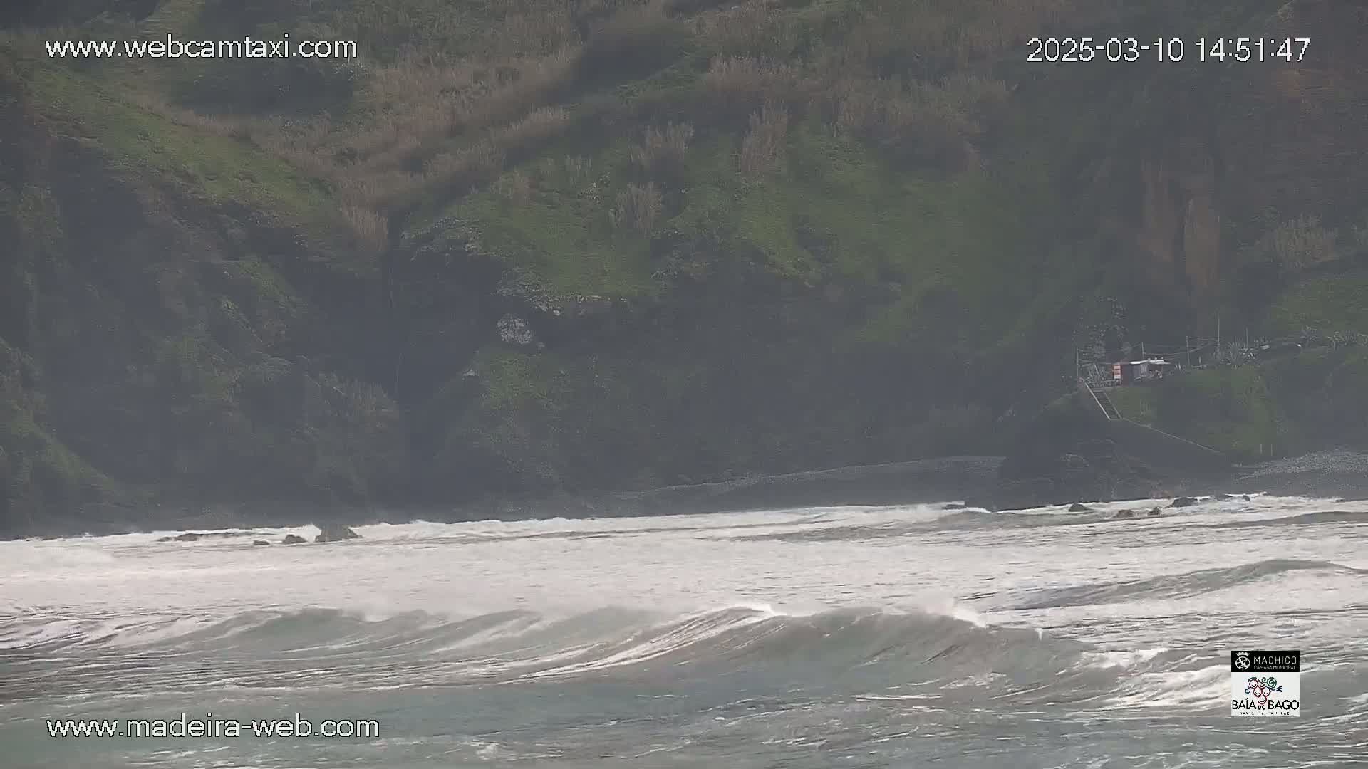 A rocky, green hillside overlooks a choppy, gray ocean with small waves under an overcast sky.
