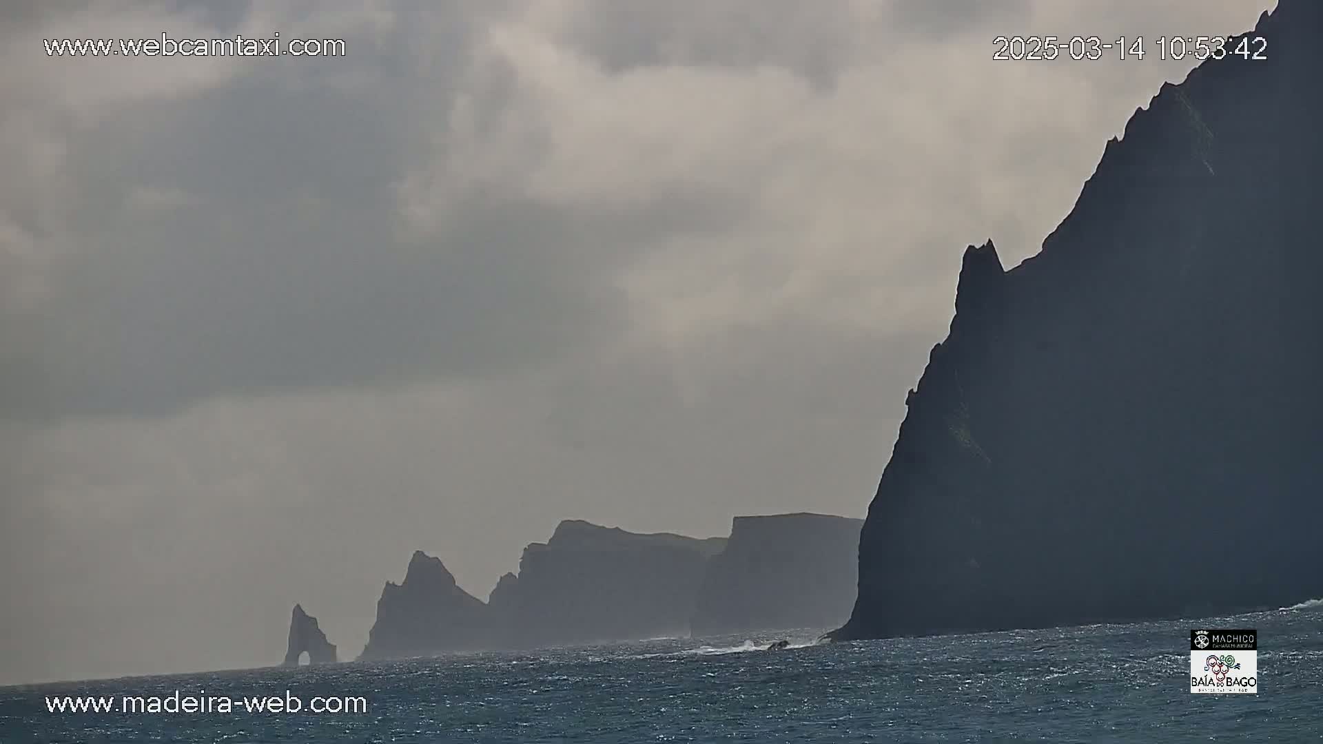 Dark, imposing cliffs rise from a choppy sea under a cloudy sky.