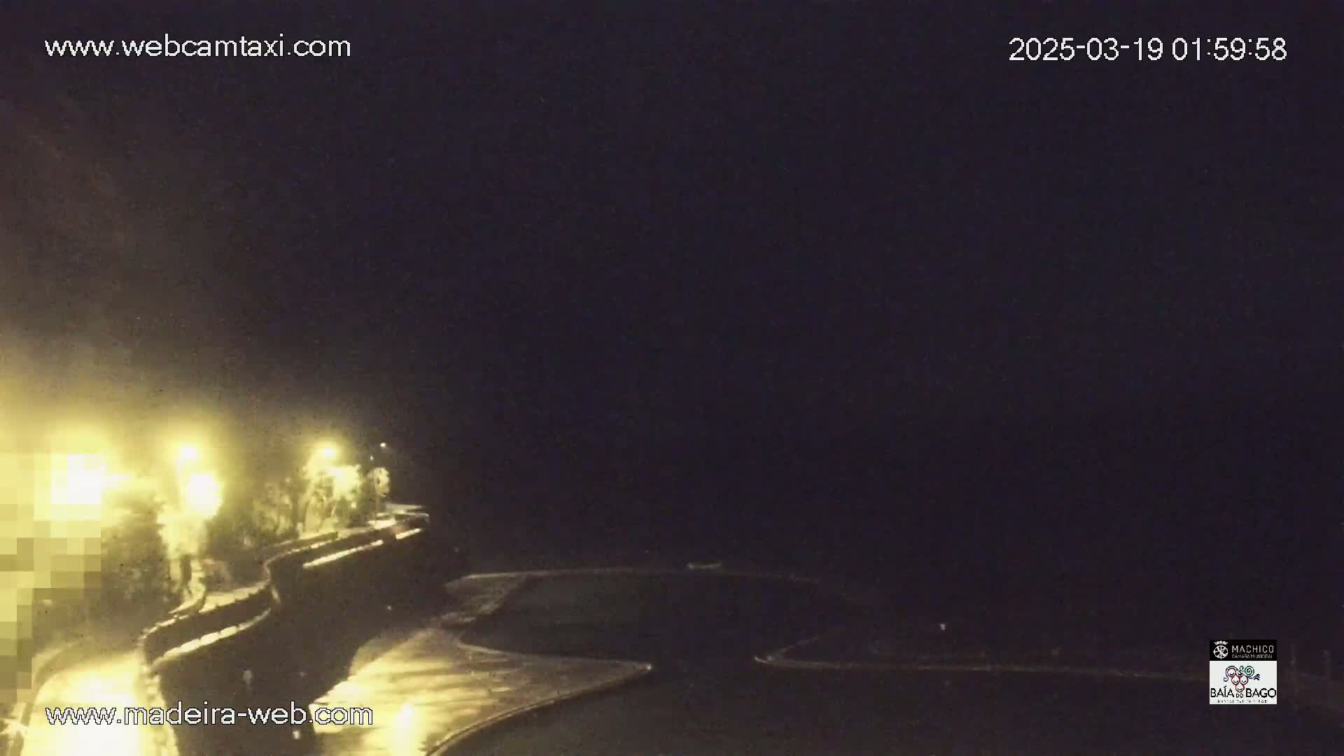 A nighttime view of a dark, possibly coastal area with some lights visible and a paved area in the foreground.