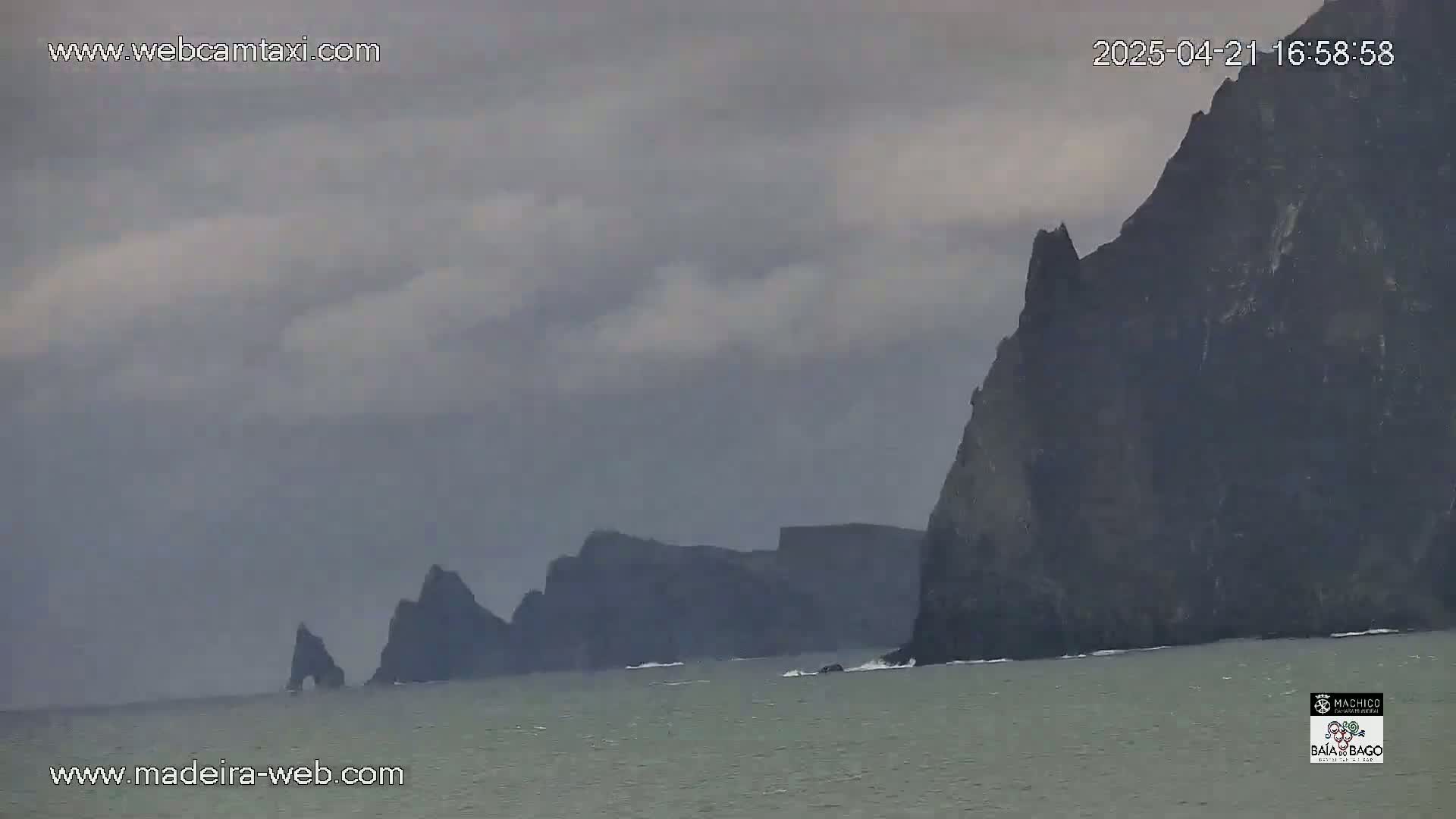 Dark, rocky cliffs rise from a gray sea under a cloudy sky.