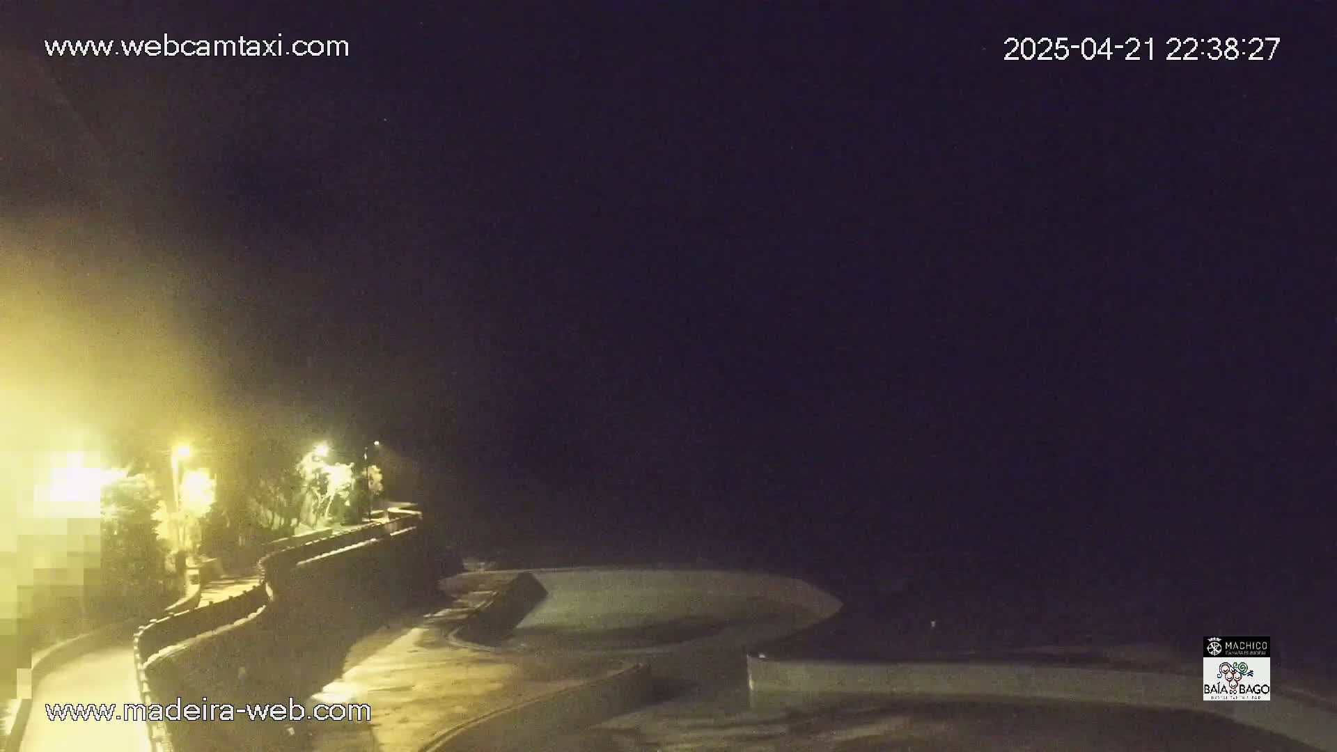 A nighttime, hazy view of a curved wall illuminated by streetlights, overlooking a dark body of water.