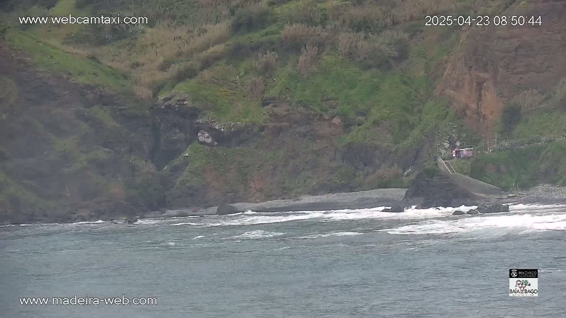 A rocky coastline with dark gray, wave-swept waters under an overcast sky.