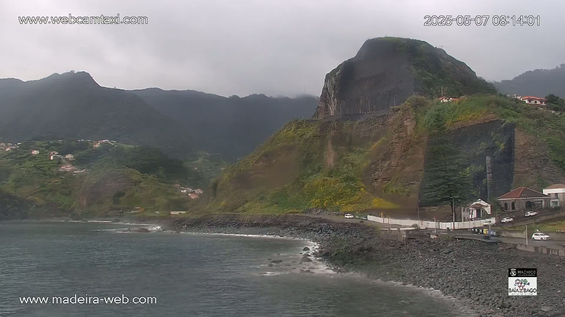 A rocky, green-covered cliff overlooking a dark-grey ocean under an overcast sky.