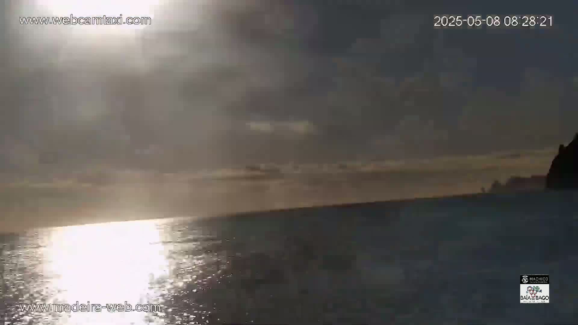A hazy sunrise over calm ocean water with a dark landmass in the distance.