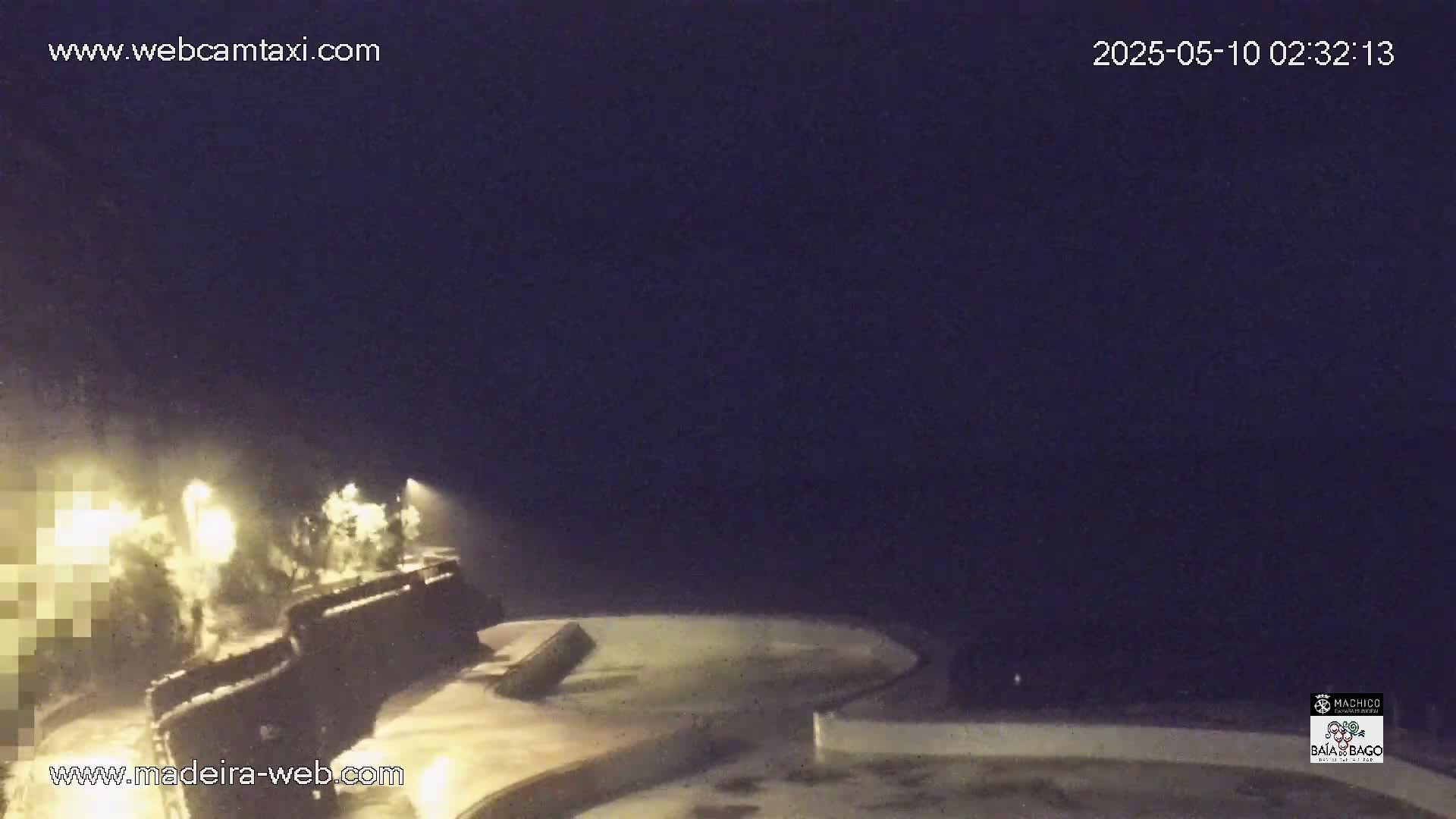 A nighttime view of a dark, possibly stormy, coast shows illuminated structures and vegetation near a water's edge.