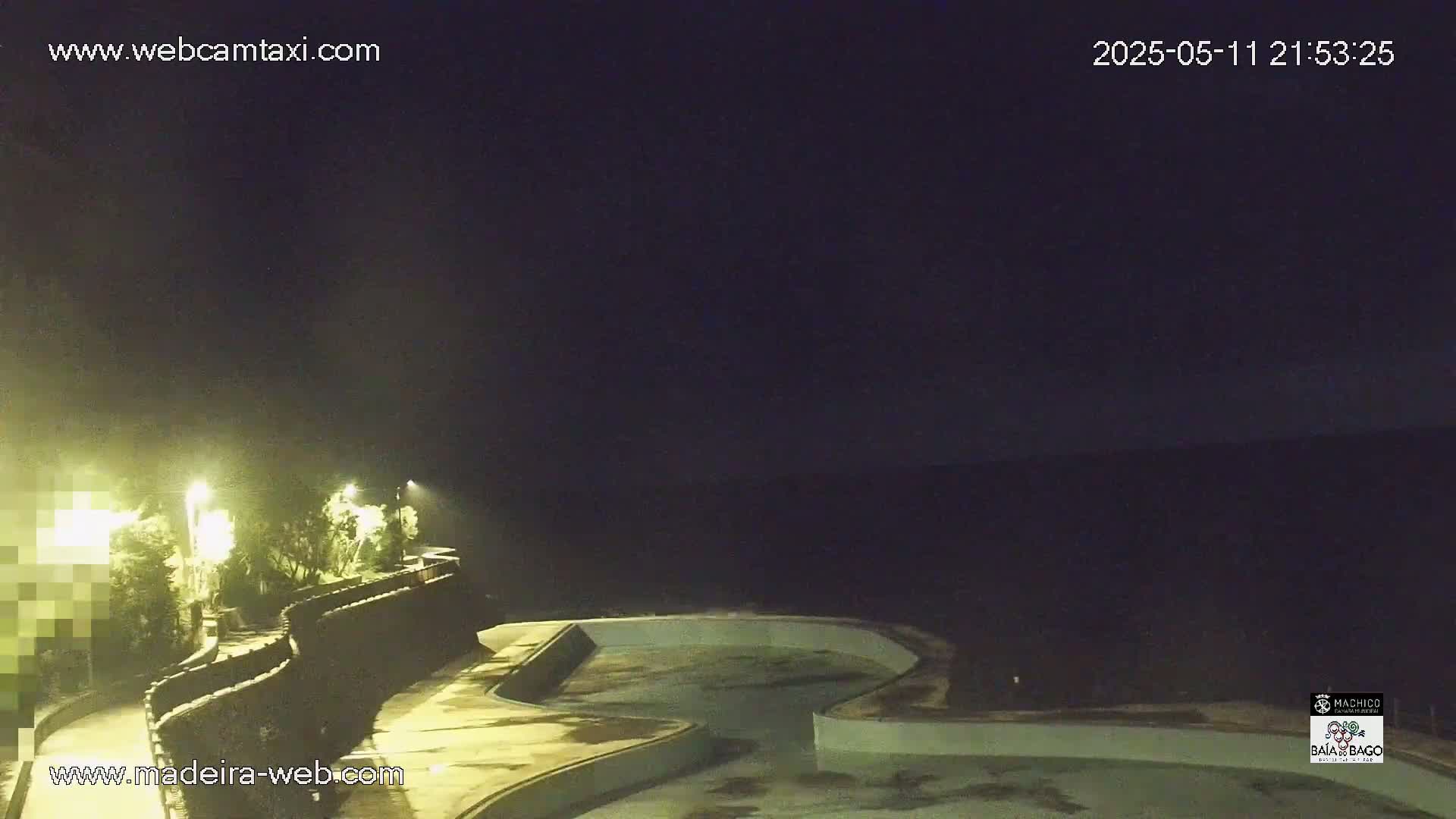 An empty, curved outdoor pool is illuminated at night under a dark sky.
