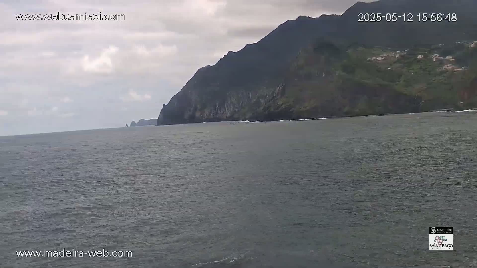 A dark-grey ocean stretches toward a steep, dark-green and grey cliffside under a mostly cloudy sky.