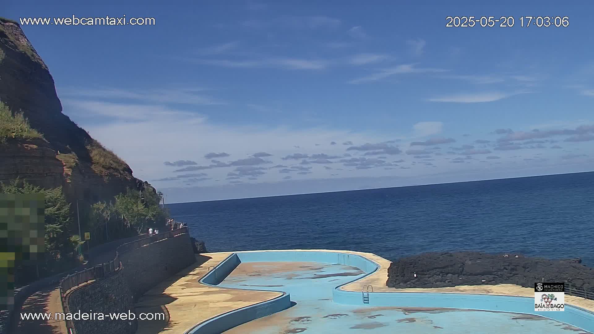 An oceanside pool with a rocky shoreline and a partly cloudy blue sky is visible.