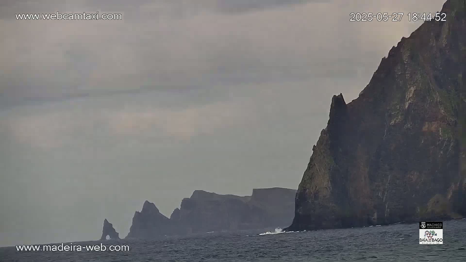 Dark, rocky cliffs rise from a gray, choppy sea under an overcast sky.
