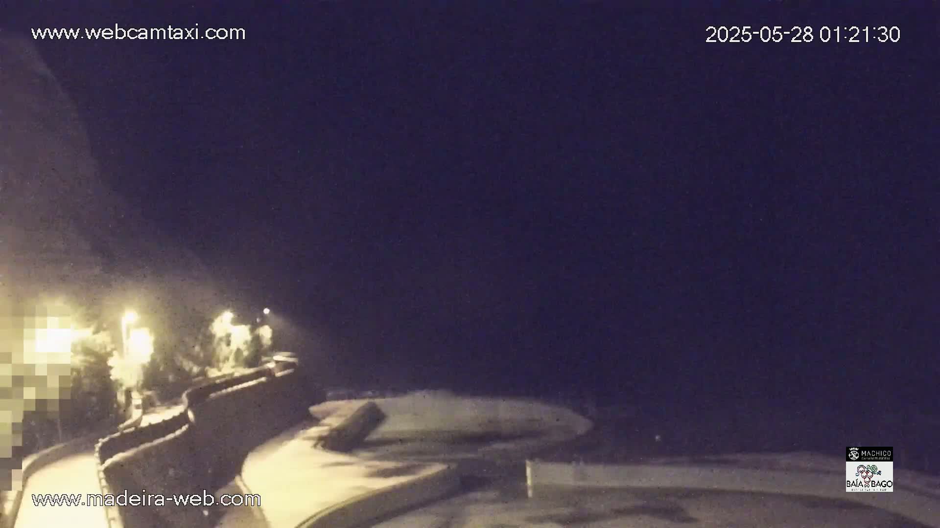 A nighttime view of a stone wall along a coastline, with some lights visible and a dark, possibly cloudy sky.