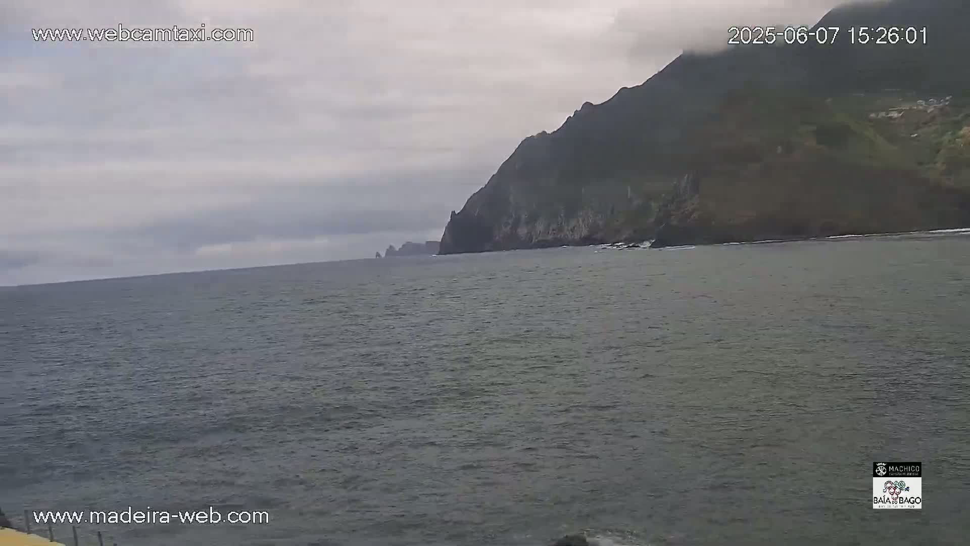 A dark gray ocean stretches to a distant, dark green cliff face under an overcast sky.