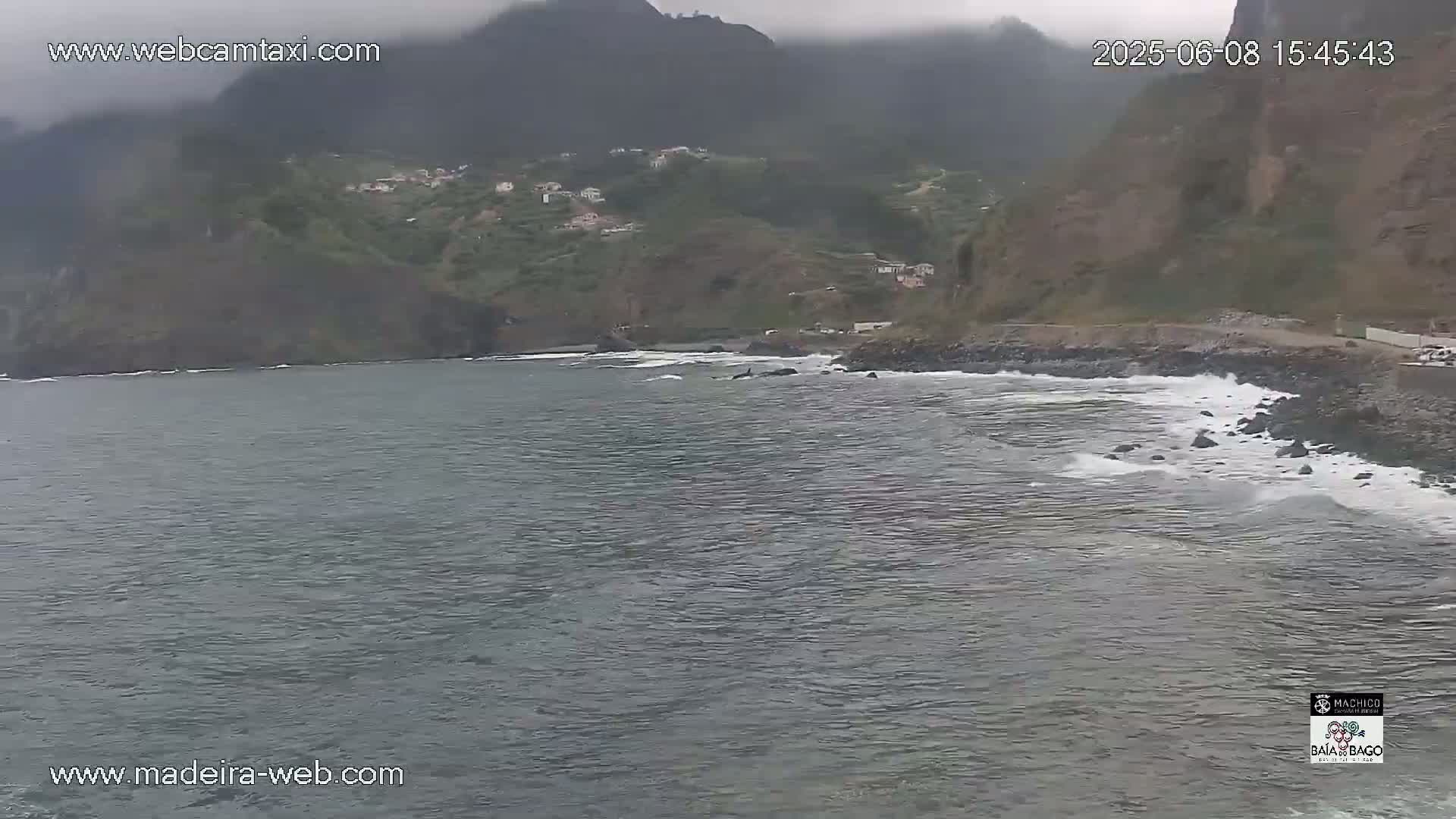 A rocky coastline with a small village nestled into the hillside is shown under an overcast sky, with gentle waves lapping at the shore.