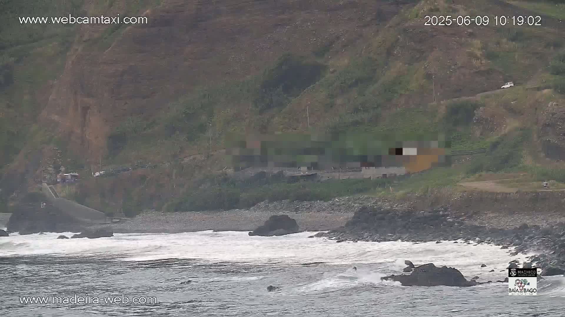 A rocky coastline with a small beach is shown, with moderate waves crashing against the shore under overcast skies.