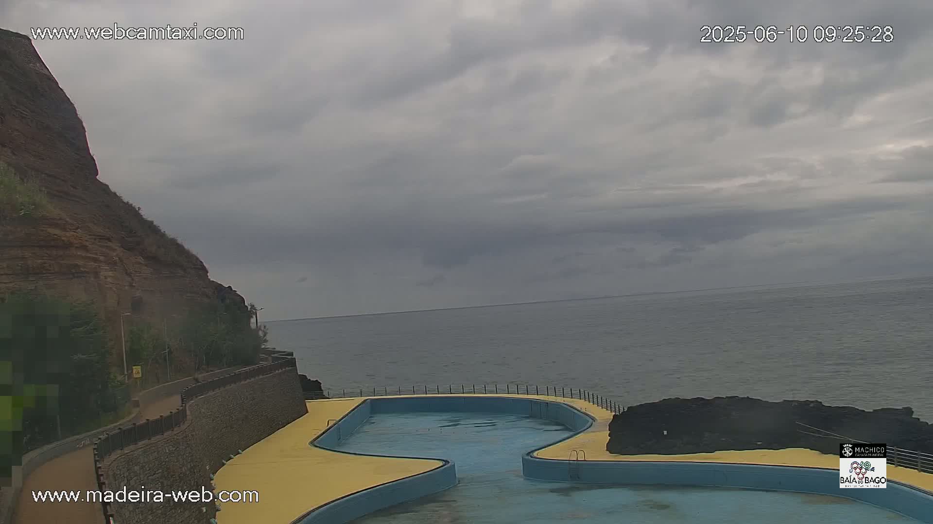 An outdoor oceanside pool sits adjacent to a cliff overlooking a calm, grey-sky ocean.