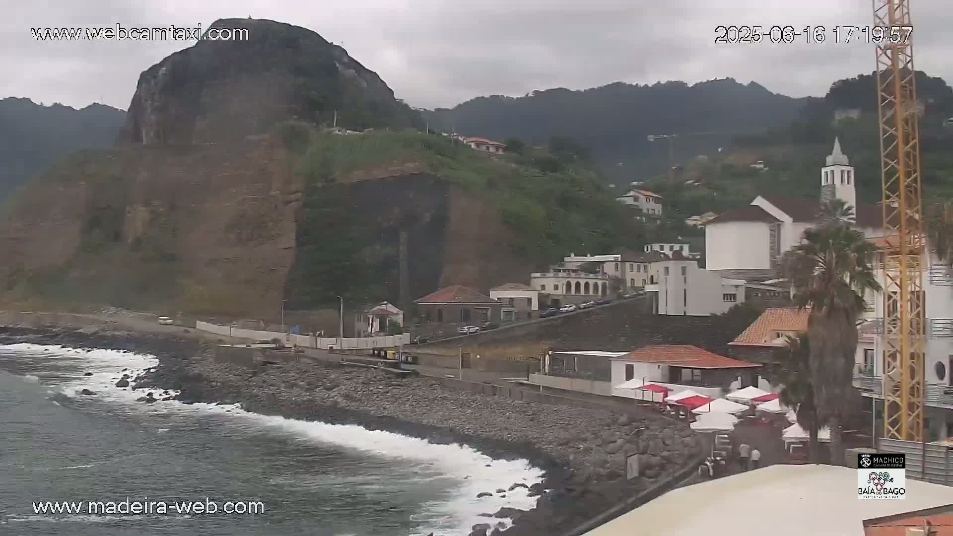A rocky coast with a town of white buildings and a large cliff behind it, under an overcast sky.