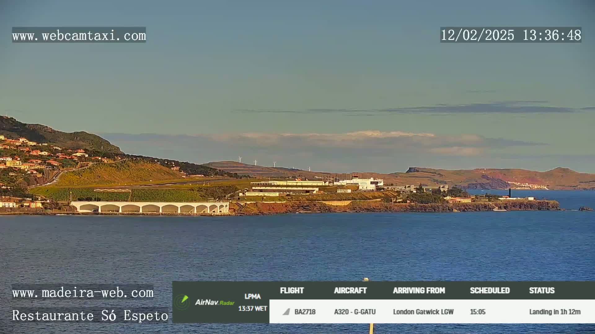 A coastal scene shows an airport, buildings, and a body of water under a mostly clear sky.