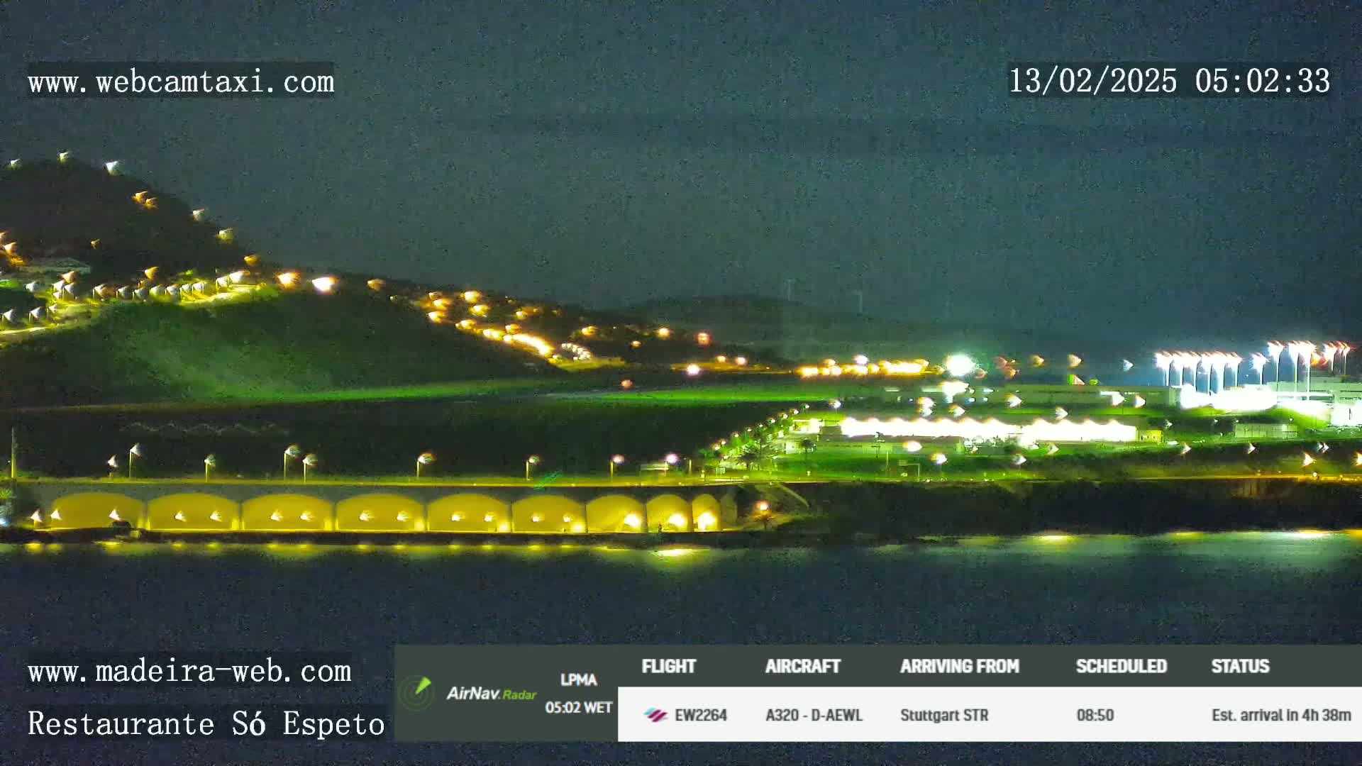 A nighttime view of a coastline with lights illuminating a hillside and buildings near the water.