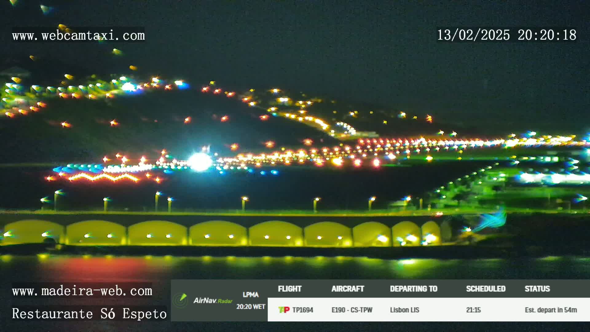 A nighttime view of an airport runway and surrounding area illuminated by lights, with a body of water visible in the foreground.