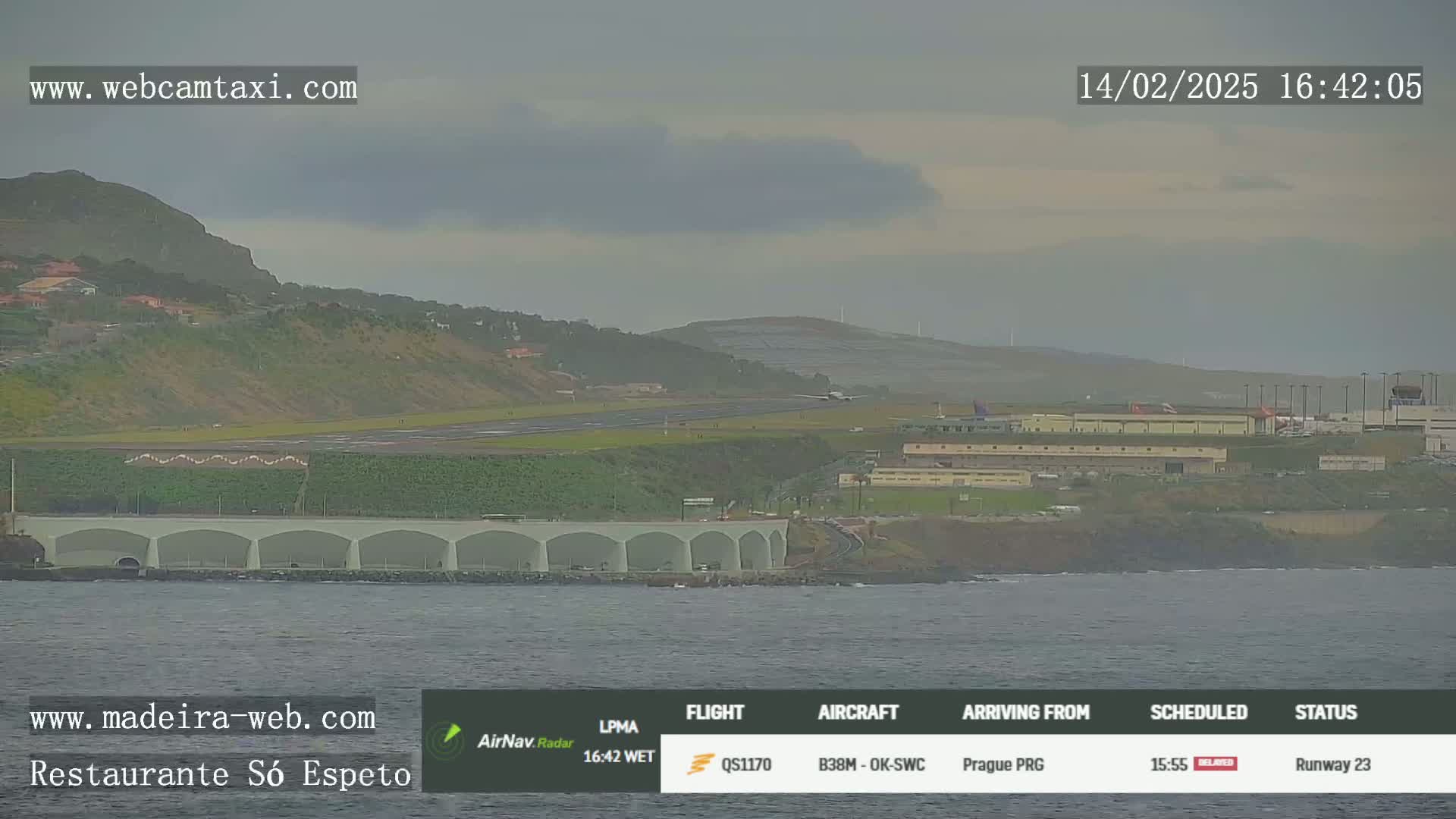 An airplane lands on a runway near a coastal town under an overcast sky.