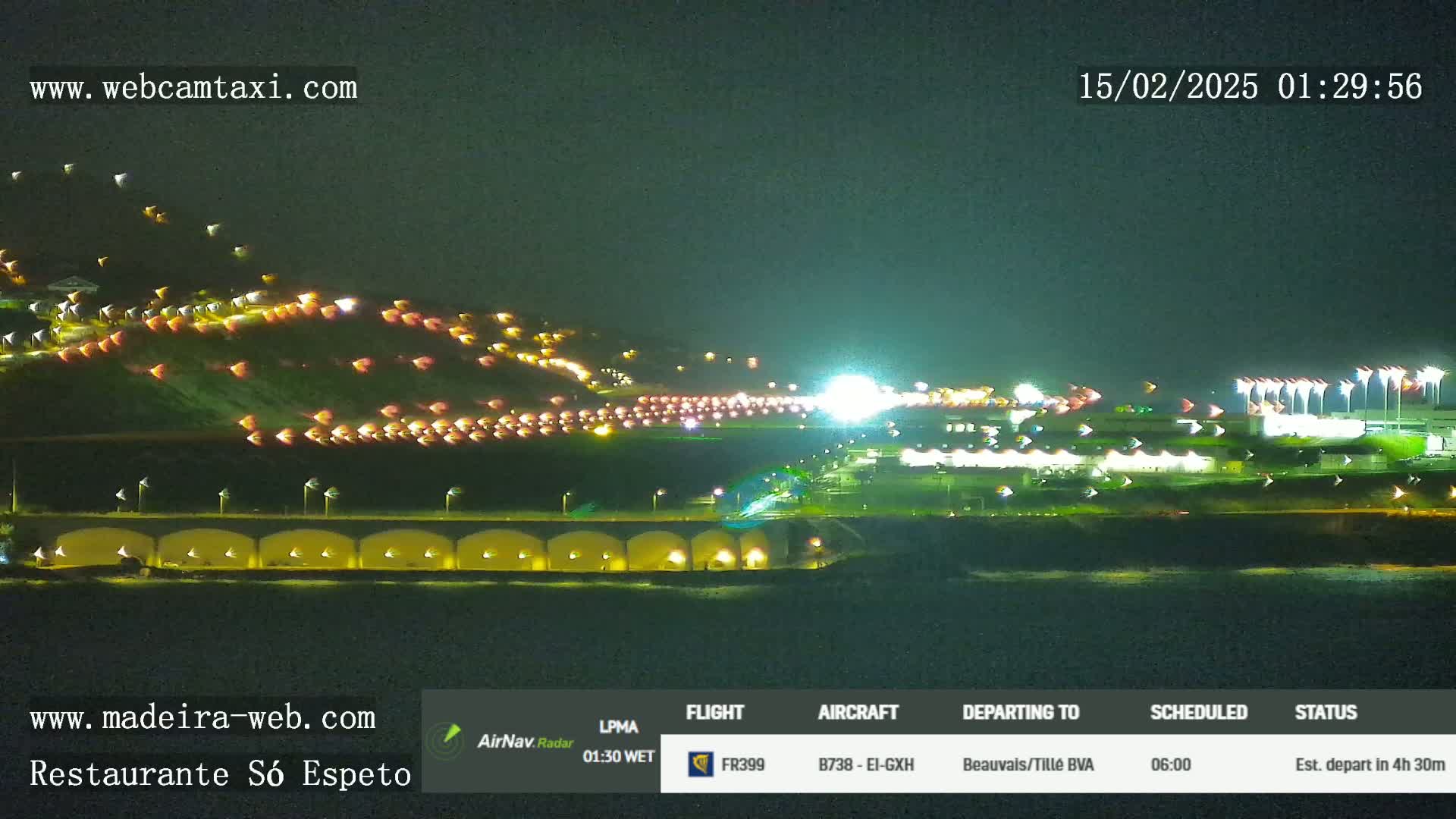 A nighttime long shot of an airport runway and surrounding area, brightly lit with numerous lights and vehicles visible.