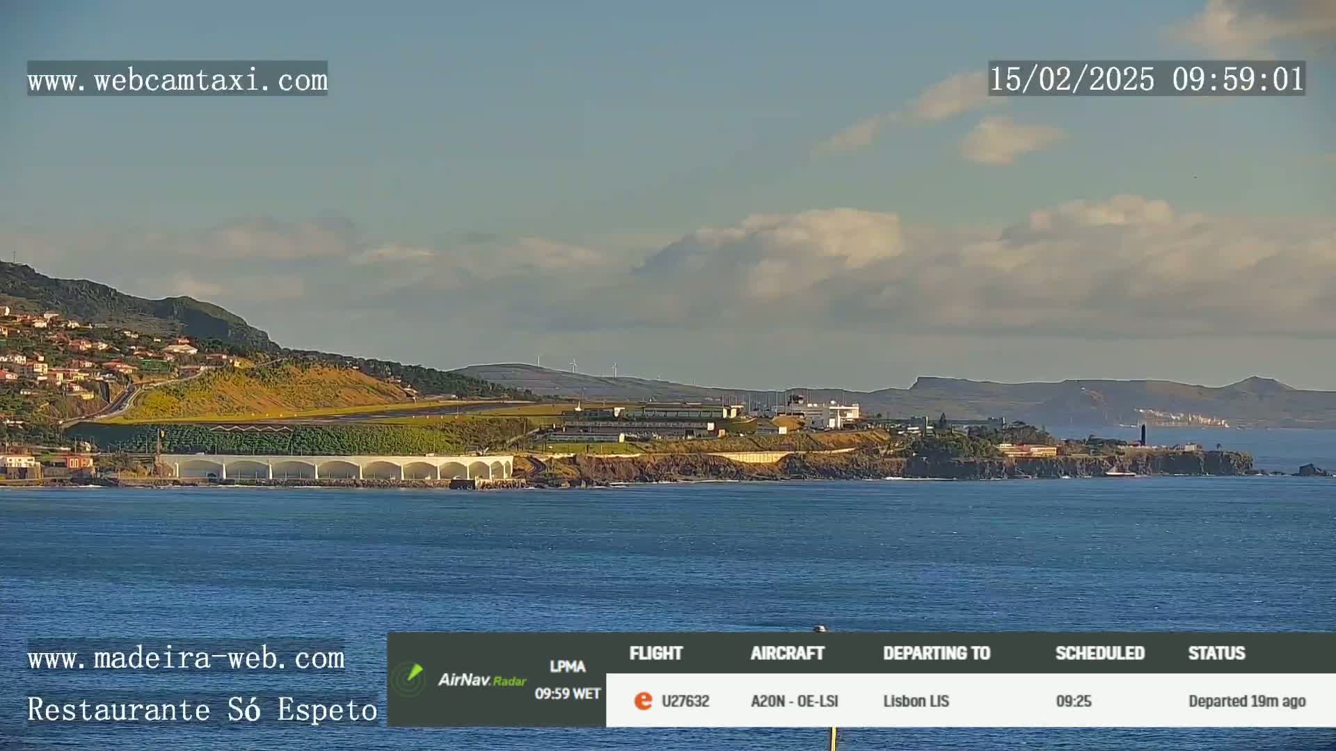 A coastal scene shows a partly cloudy sky over an airport, buildings, and calm ocean water.