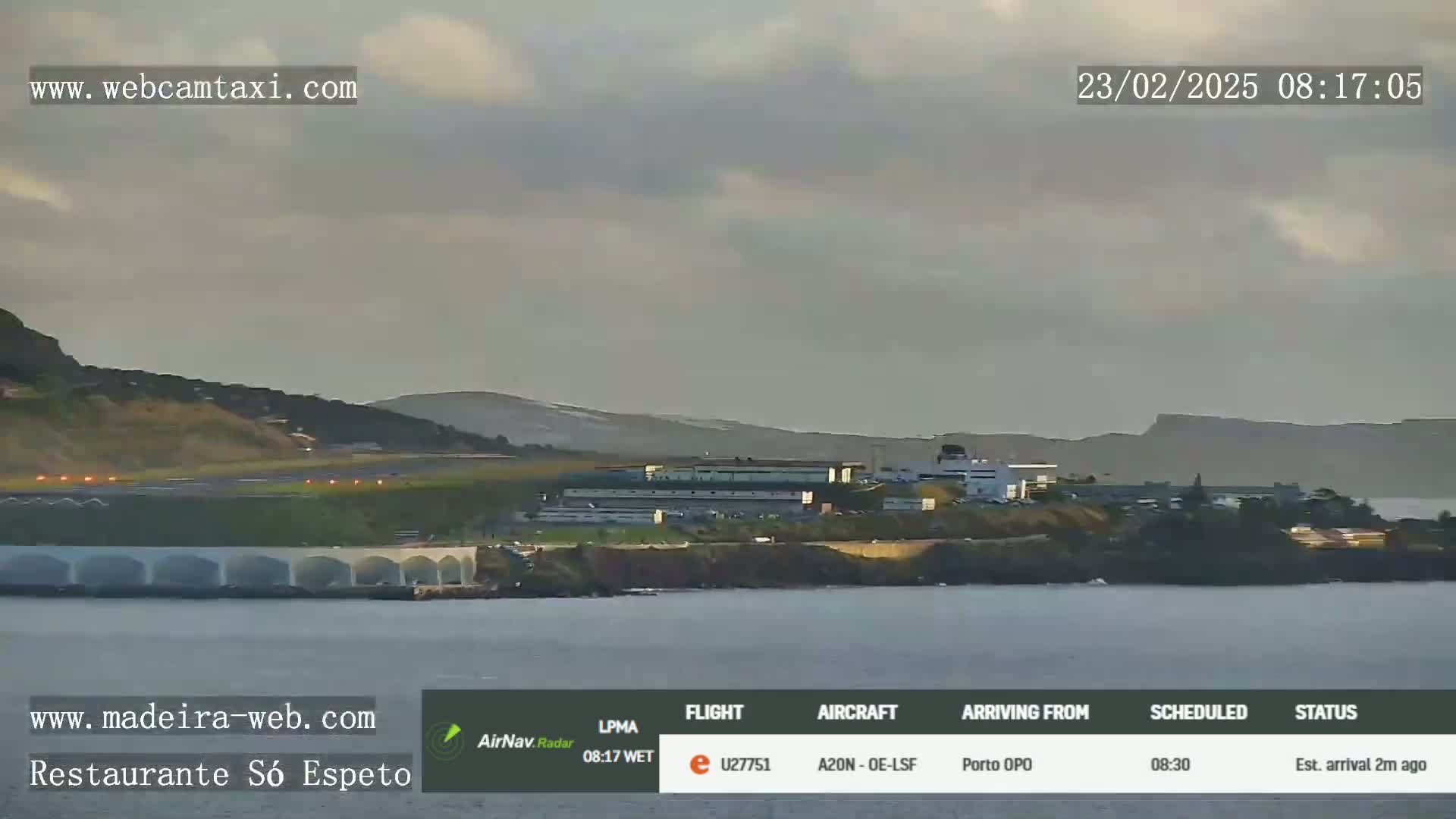 A long shot shows an airport and calm body of water under an overcast sky.