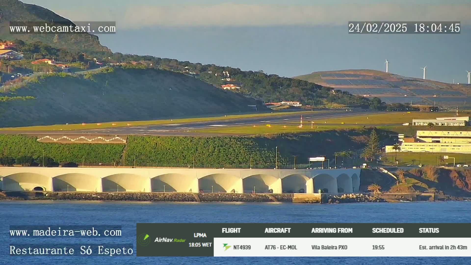 An airport runway and surrounding buildings are visible from a coastal vantage point, under clear skies at sunset.