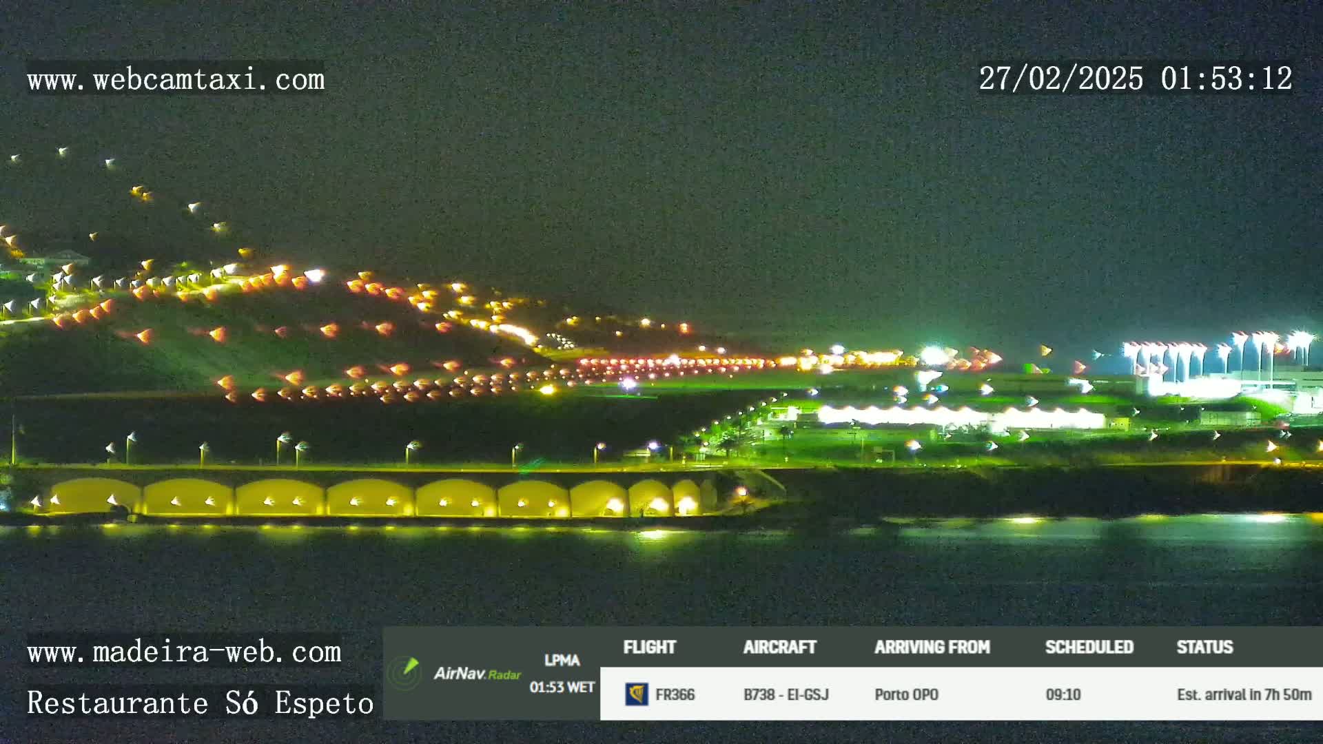 A nighttime view of a brightly lit airport and coastline, with calm water.