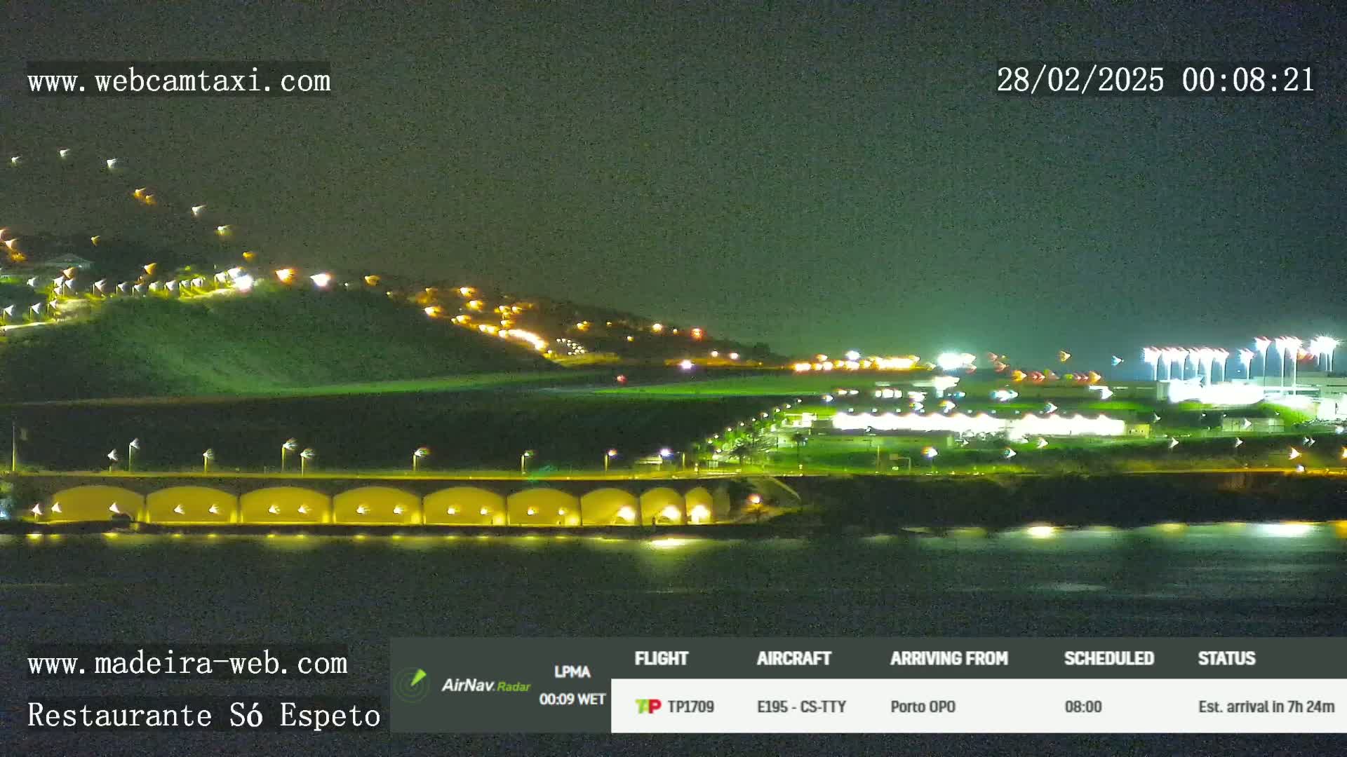 A nighttime view of a coastline with illuminated buildings on a hill and airport lights in the foreground, under a clear dark sky.