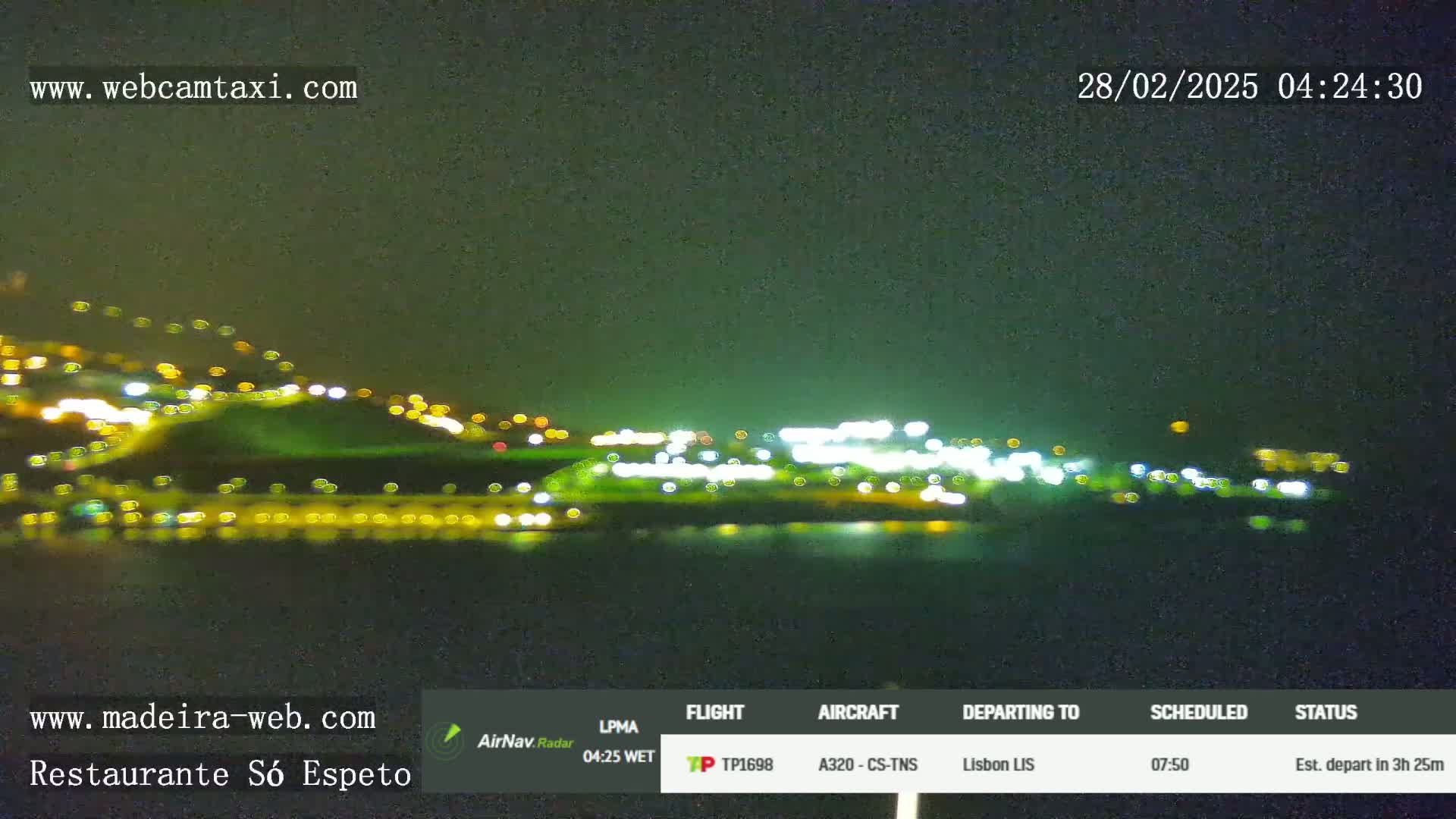 A nighttime, blurry view of a city's lights across a body of water under a dark sky.