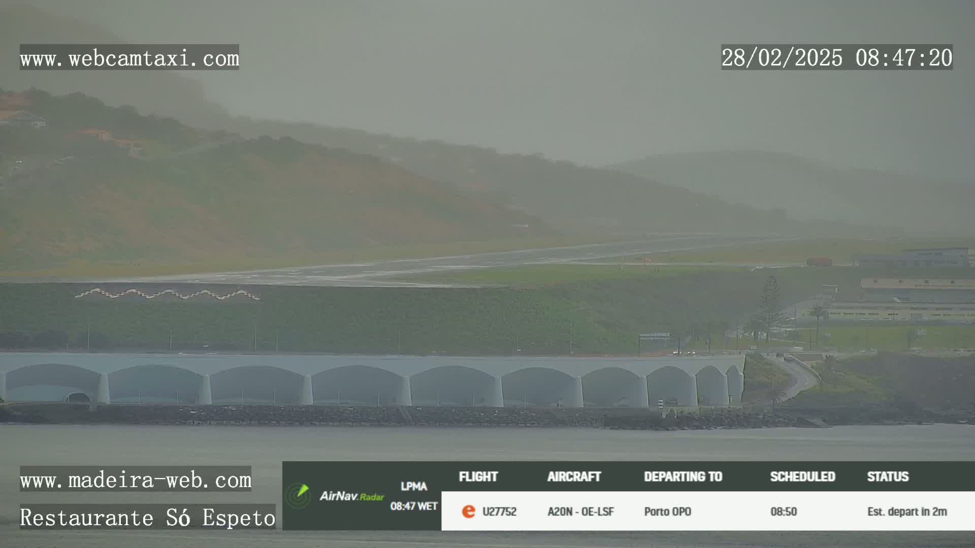 A hazy, overcast day shows an airport runway and terminal buildings next to a body of water.