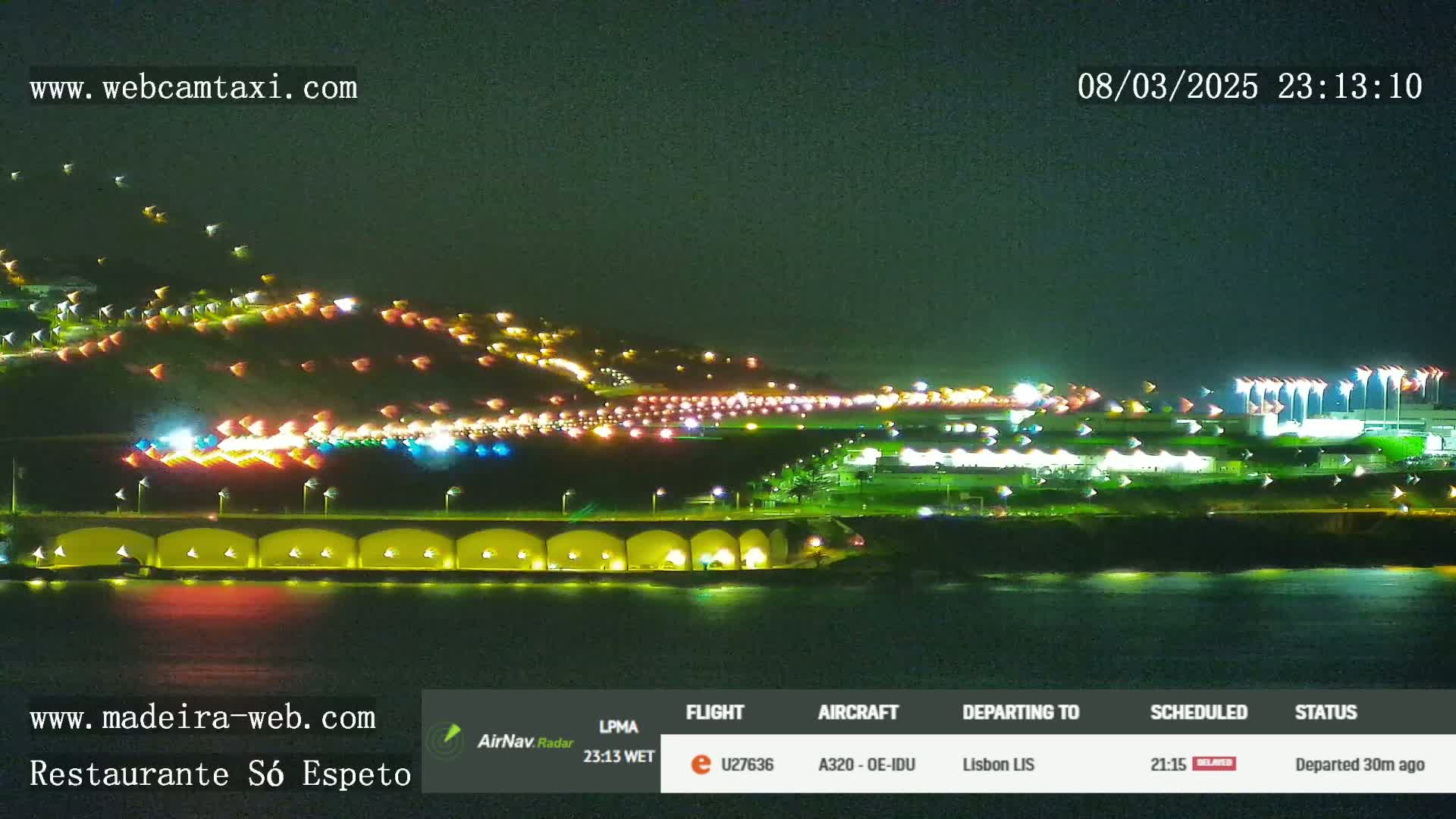 A nighttime long shot of a brightly lit airport and coastline, with the water appearing calm.