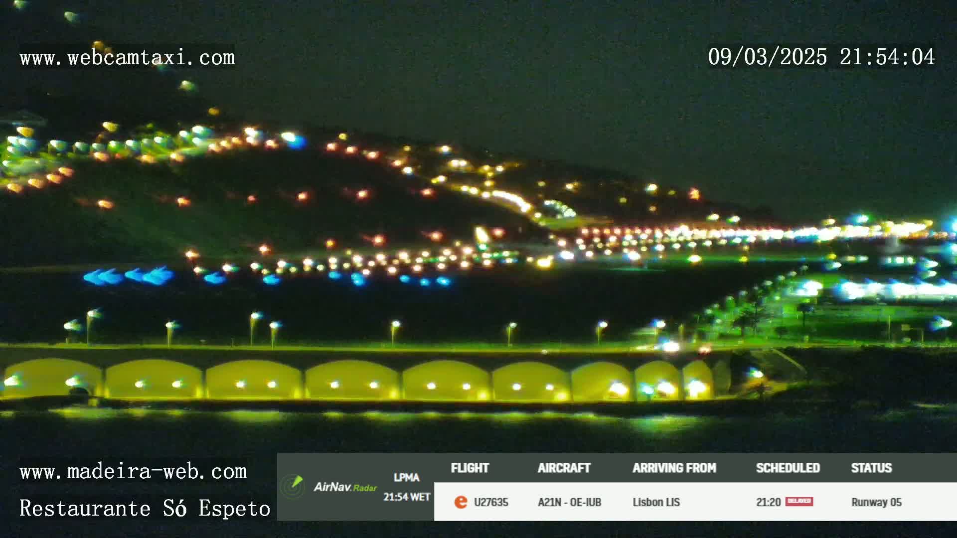 A nighttime view of a brightly lit coastal town and a bridge, with numerous lights visible along a waterfront.