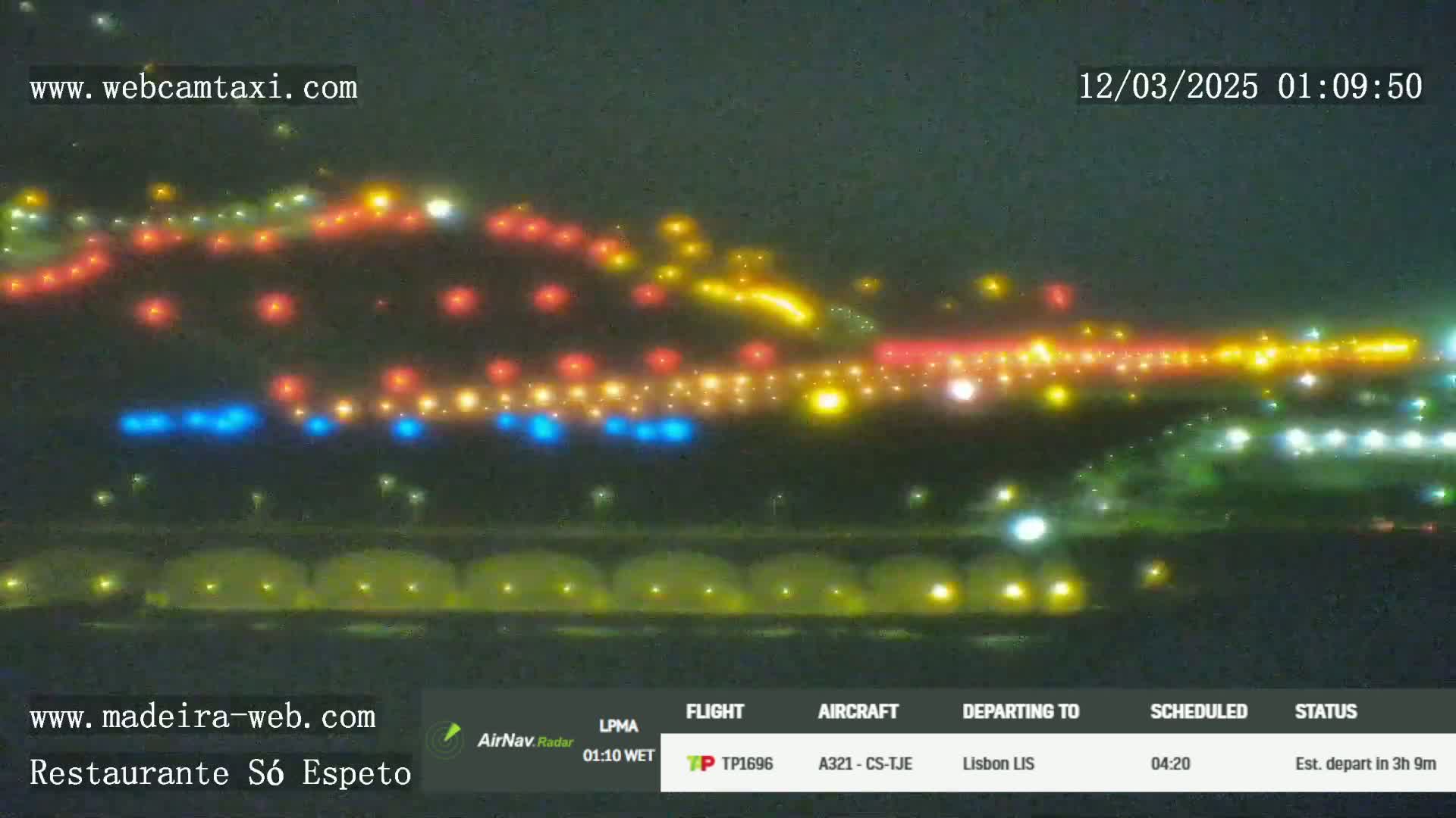 A nighttime view of an airport runway with multicolored lights illuminating the tarmac and surrounding area under hazy conditions.