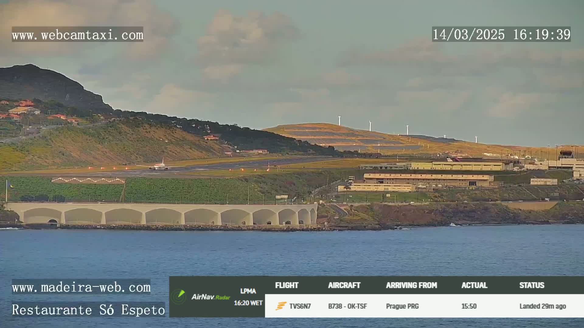 An airplane has just landed on a runway near a coastline, under partly cloudy skies.