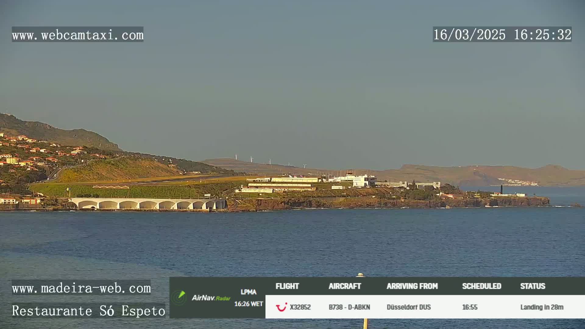 A coastal airport with a runway and buildings is seen from across the water on a clear day.