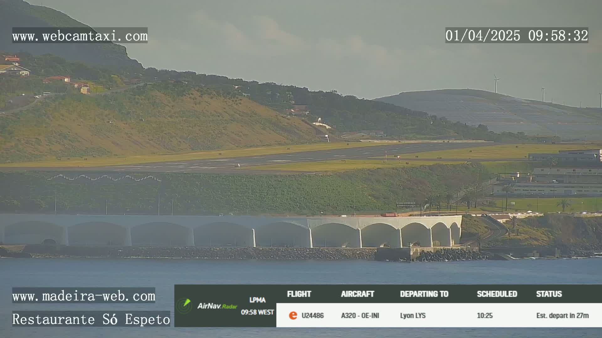 An airport runway and terminal are visible near a coastline, with a partly cloudy sky.