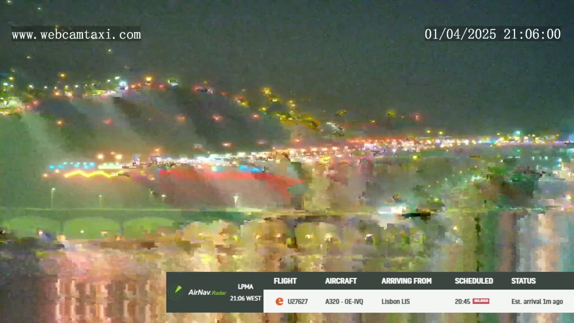 A nighttime, blurry view of a brightly lit city skyline and a bridge, possibly near an airport, under cloudy conditions.