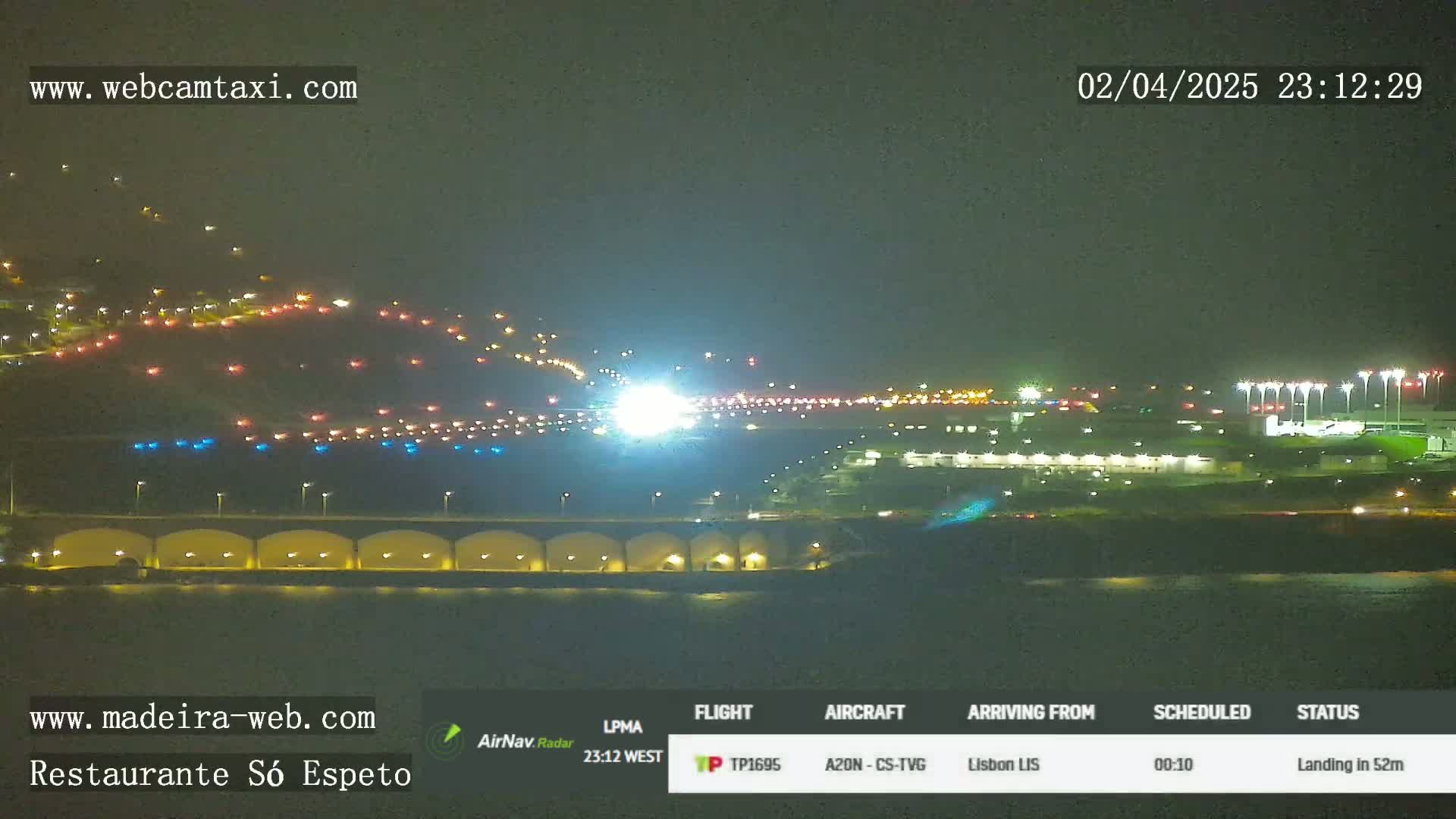 A brightly lit airplane is landing on a runway at night near a body of water.