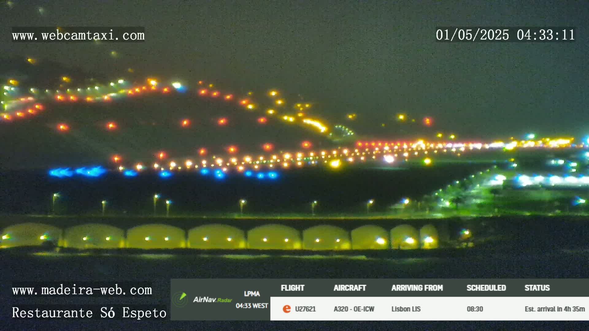 A nighttime long shot of an airport runway illuminated with various colored lights, under a dark sky.