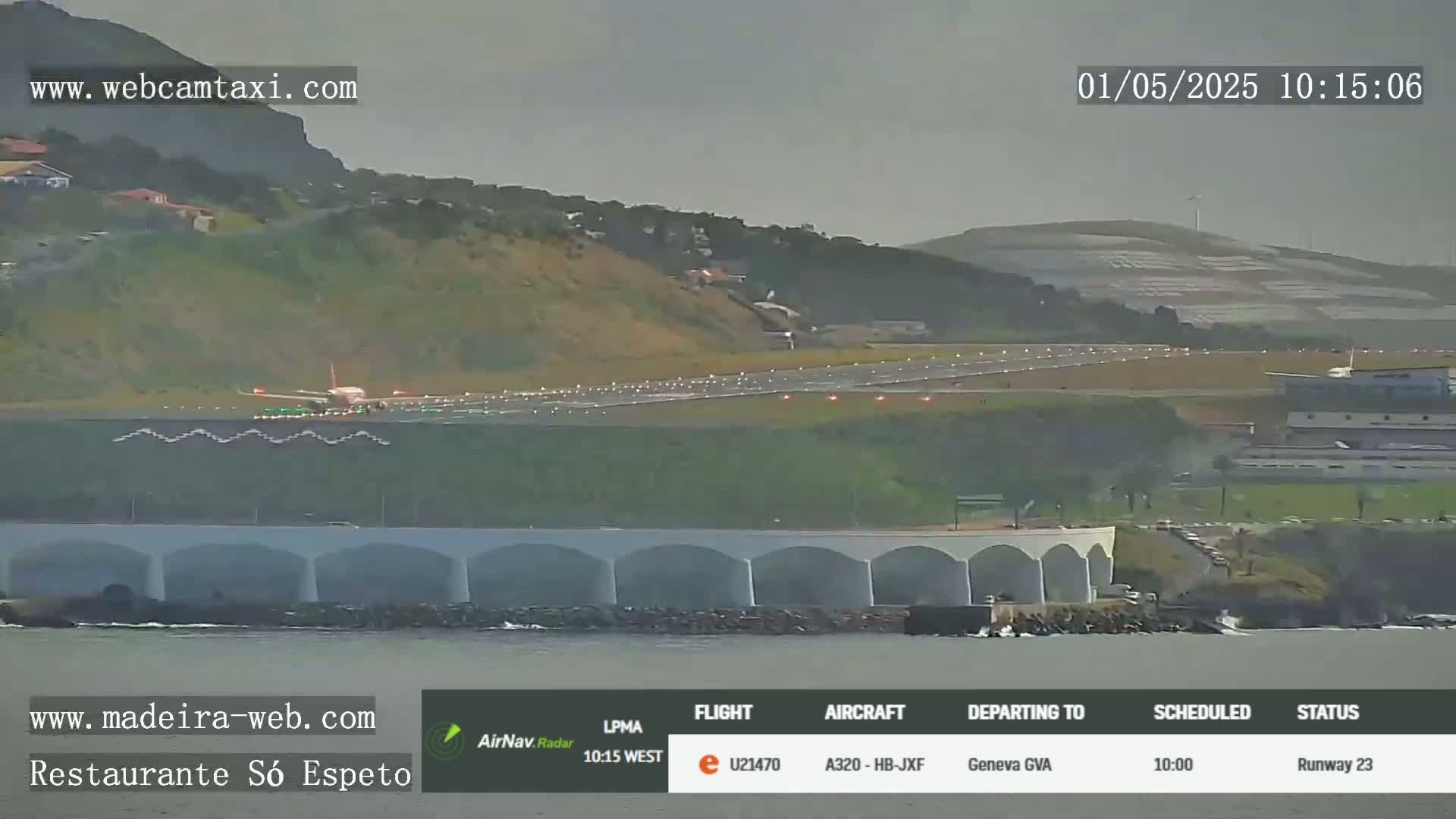 A plane is taking off from an airport runway near a body of water under overcast skies.