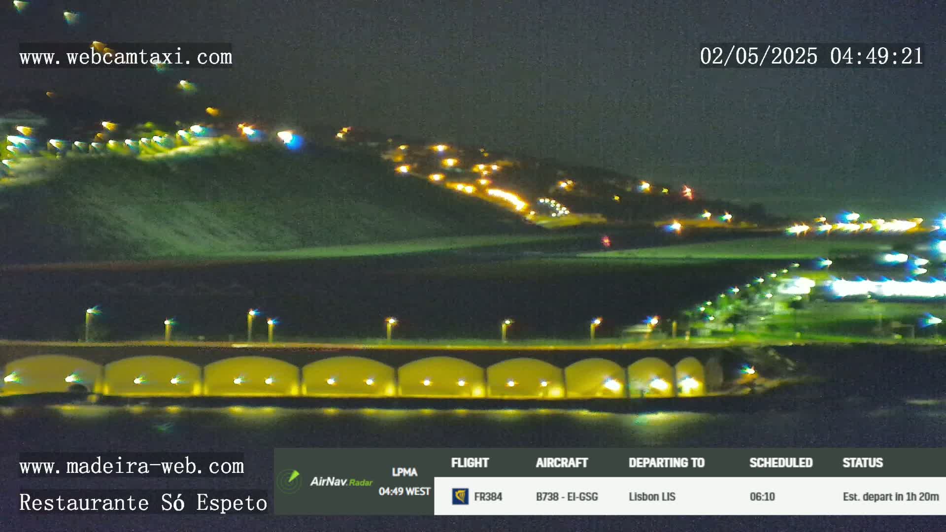 A nighttime view of a hilltop with illuminated buildings, a bridge with lights underneath, and a dark body of water.
