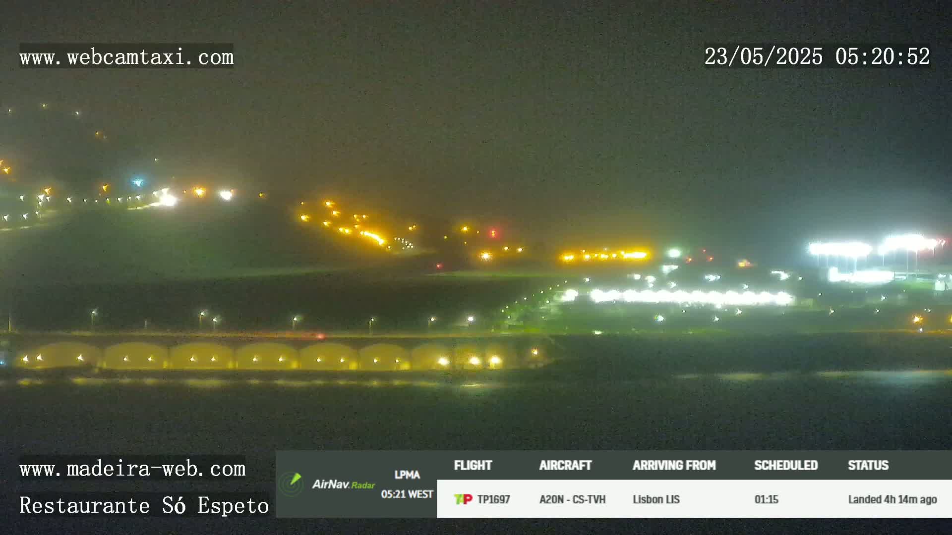A nighttime, hazy view of a coastline with illuminated buildings and structures, including what appears to be a stadium or sports field.