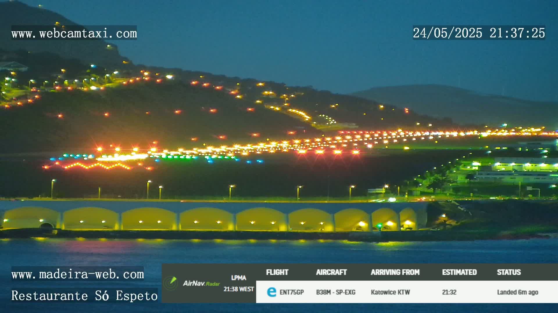 A nighttime view of an airport runway illuminated with lights, situated along a hillside overlooking the ocean.
