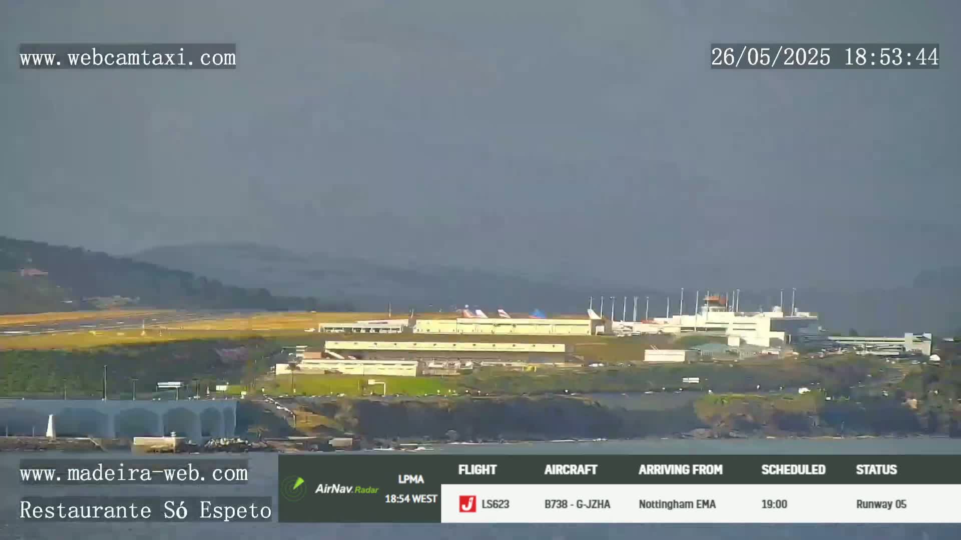 An airport is shown on an overcast day, situated near a body of water and hills.