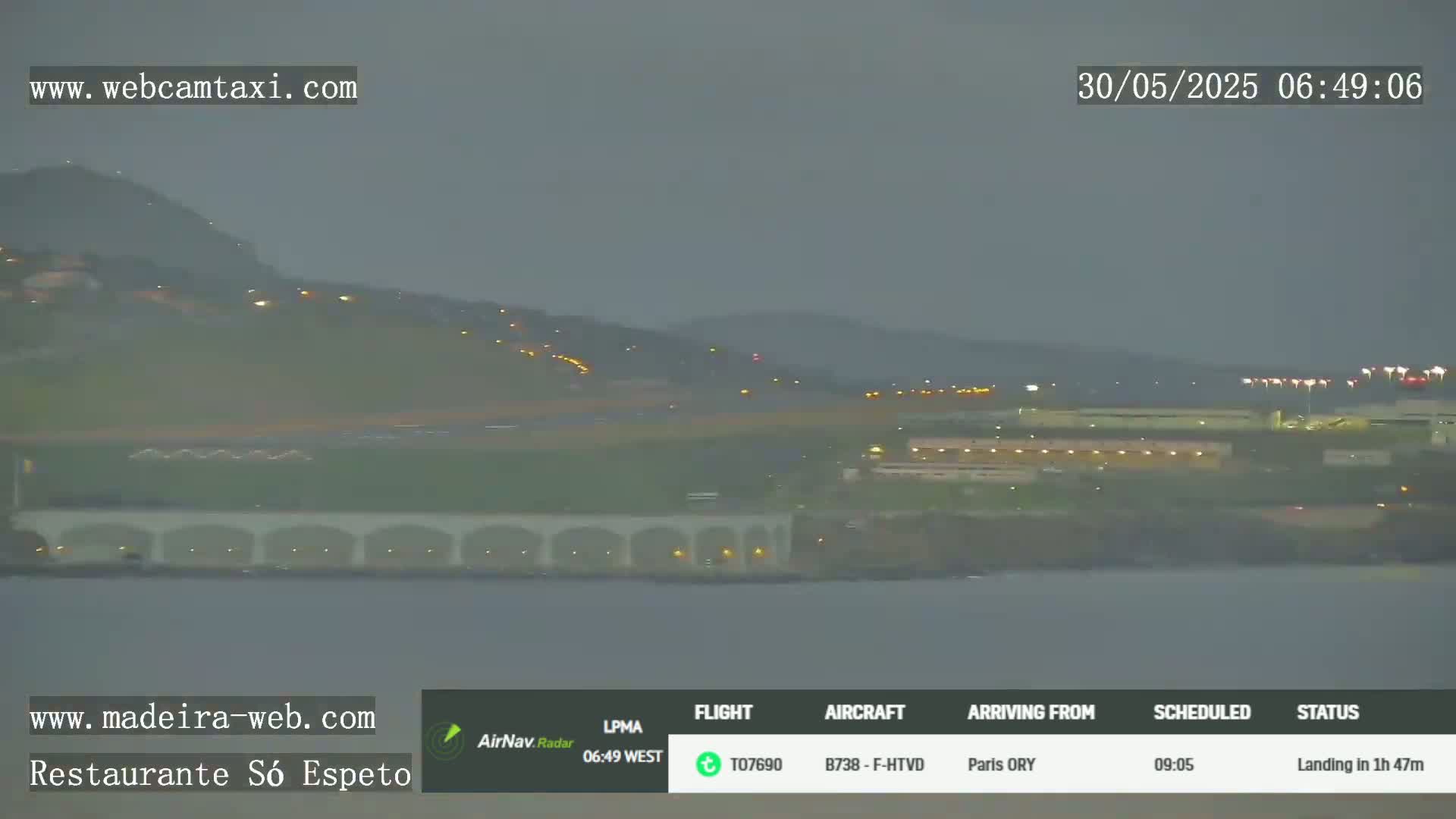 A dimly lit airport runway and surrounding buildings are visible under an overcast sky.