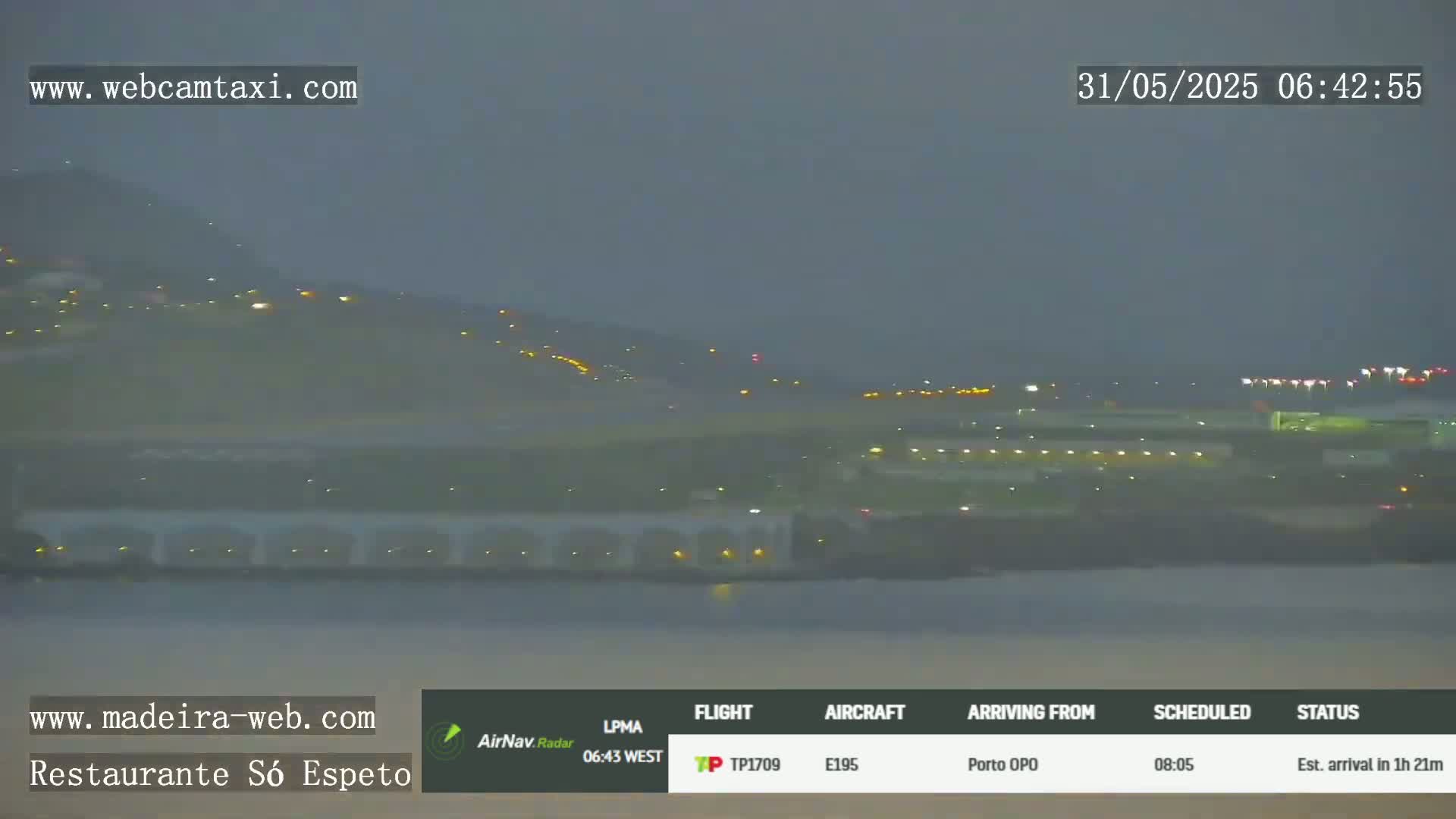 A nighttime long shot of an airport runway and surrounding area, with a hazy or overcast sky.
