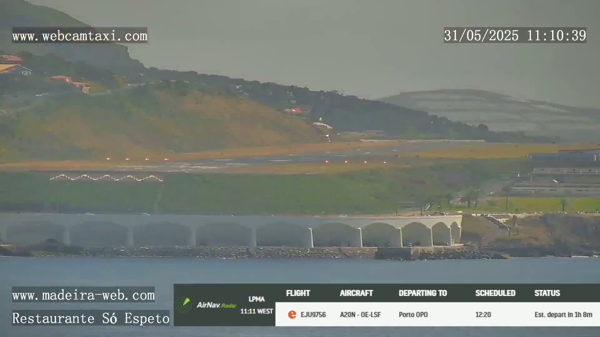 A distant airplane is on a runway at an airport near the ocean under hazy, overcast skies.